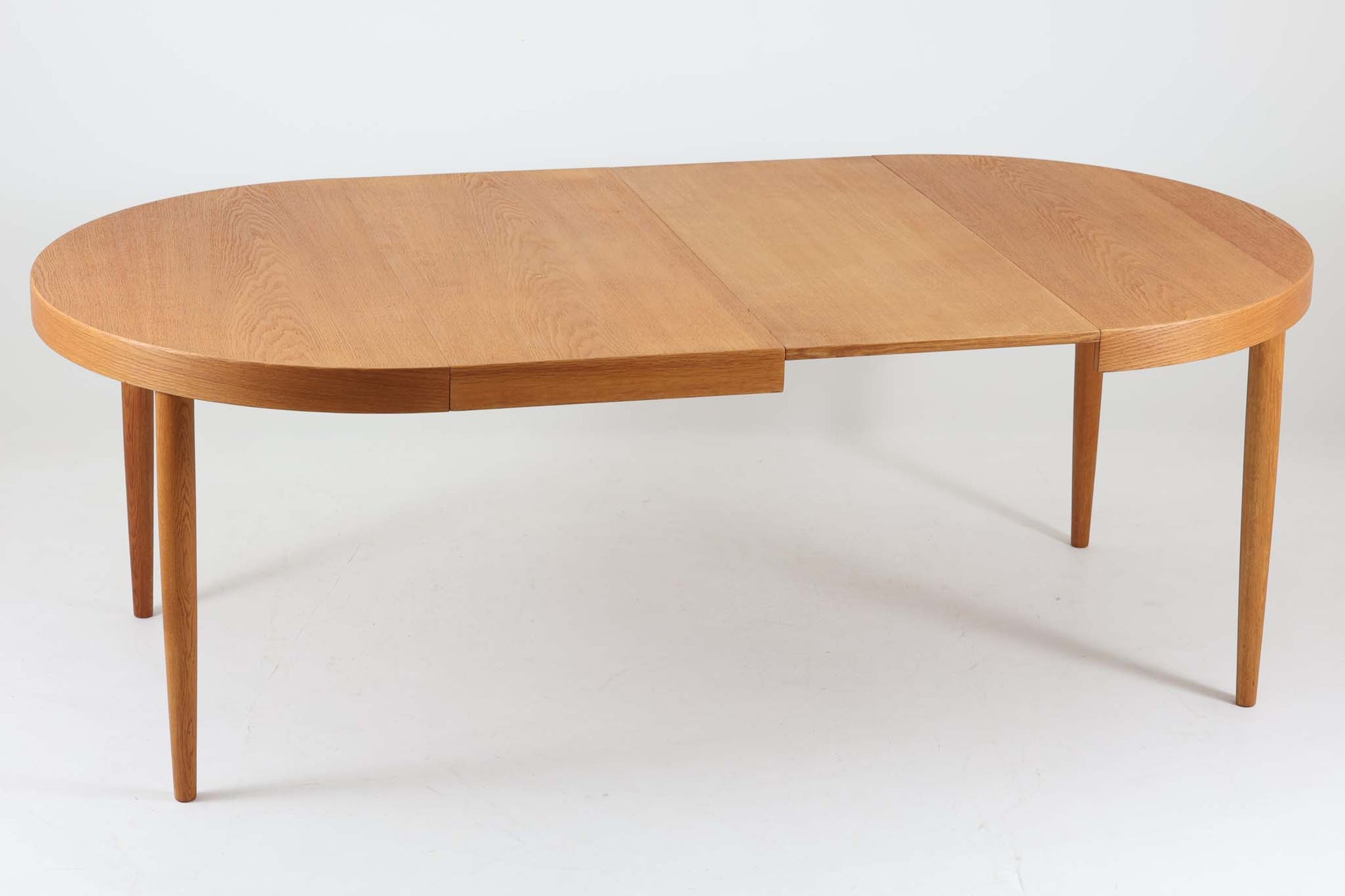 美しい木目のオーク材で作られたデンマーク製のビンテージダイニングテーブルです。シンプルでありながら北欧らしい洗練されたデザインが魅力で、エクステンション機能により天板を伸長して大人数にも対応可能です。天板を閉じた状態では直径のある円形テーブルとして、拡張時には楕円形になり広々とご使用いただけます。丸みを帯びた天板のエッジと先細りの脚が軽やかで、どんな空間にも調和します。Danish Controlの刻印も確認でき、品質の高さが伺える逸品です。北欧モダンな空間演出におすすめの一台です。