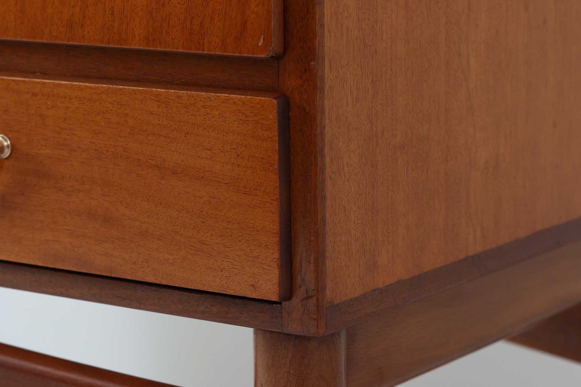 FDBモブラーでBorge mogensenの後任としてアートディレクターを務めたPoul m. Voltherによる、美しく洗練されたキャビネット。良質なマホガニー材の本体に、ビーチ材の脚部を組み合わせたコントラストが魅力です。真鍮の丸い鍵穴が特徴的な3枚の扉を備え、中央には調節可能な棚、両側には精巧な蟻継ぎが施された移動式の引き出しを配しています。下部には真鍮の俵型ハンドル付きの引き出しが3杯並び、細部へのこだわりが際立ちます。また、室内で靴を履く文化に配慮し、脚先には汚れ防止のための濃い塗装が施されています。1950年代にデザインされた本作は、先細りの脚やストレッチャーがミニマルな美しさを際立たせる一方、シンメトリーなフォルムや真鍮の装飾が伝統的なエレガンスを醸し出し、モダンとクラシックが調和した逸品です。