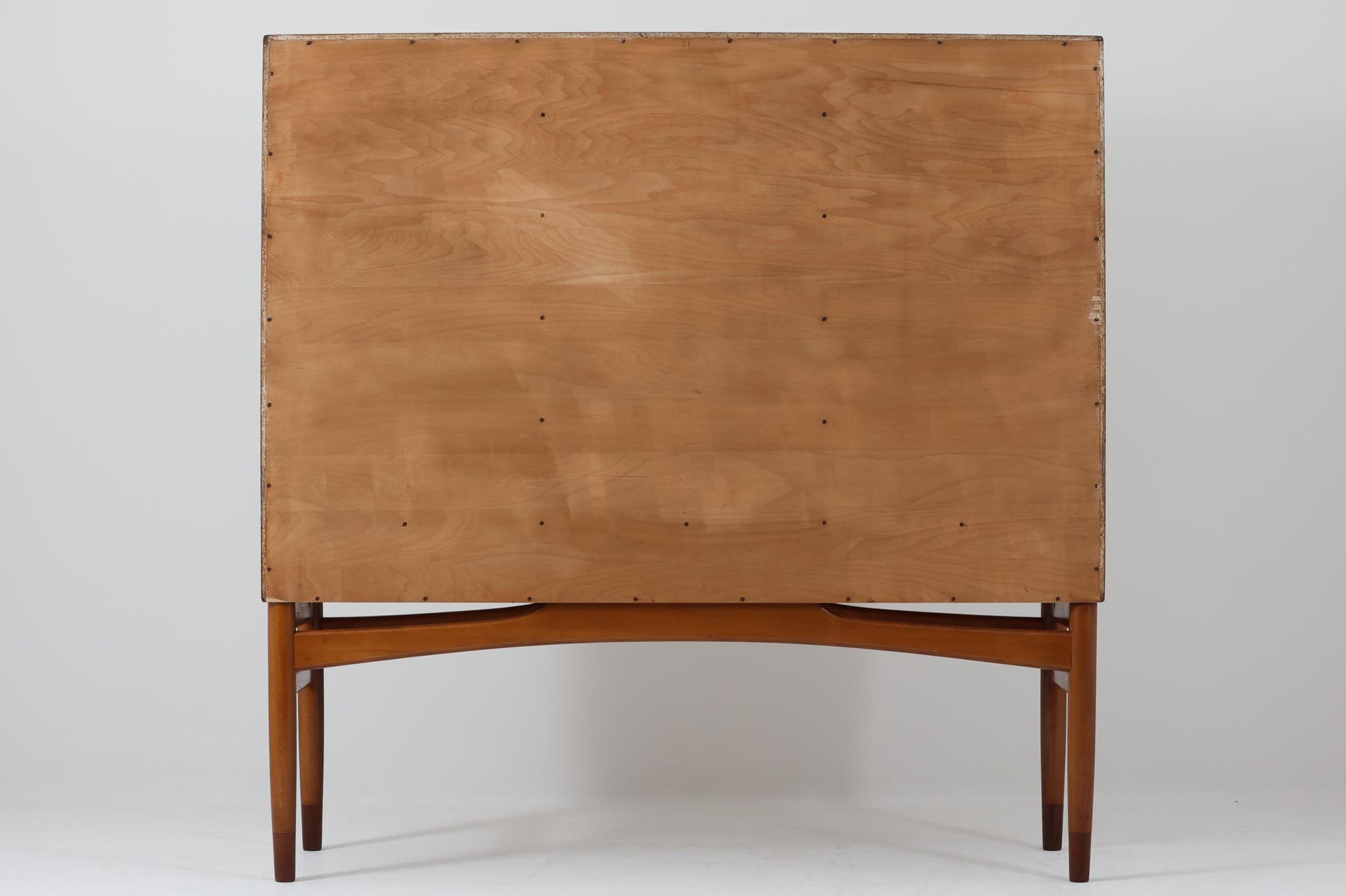 FDBモブラーでBorge mogensenの後任としてアートディレクターを務めたPoul m. Voltherによる、美しく洗練されたキャビネット。良質なマホガニー材の本体に、ビーチ材の脚部を組み合わせたコントラストが魅力です。真鍮の丸い鍵穴が特徴的な3枚の扉を備え、中央には調節可能な棚、両側には精巧な蟻継ぎが施された移動式の引き出しを配しています。下部には真鍮の俵型ハンドル付きの引き出しが3杯並び、細部へのこだわりが際立ちます。また、室内で靴を履く文化に配慮し、脚先には汚れ防止のための濃い塗装が施されています。1950年代にデザインされた本作は、先細りの脚やストレッチャーがミニマルな美しさを際立たせる一方、シンメトリーなフォルムや真鍮の装飾が伝統的なエレガンスを醸し出し、モダンとクラシックが調和した逸品です。