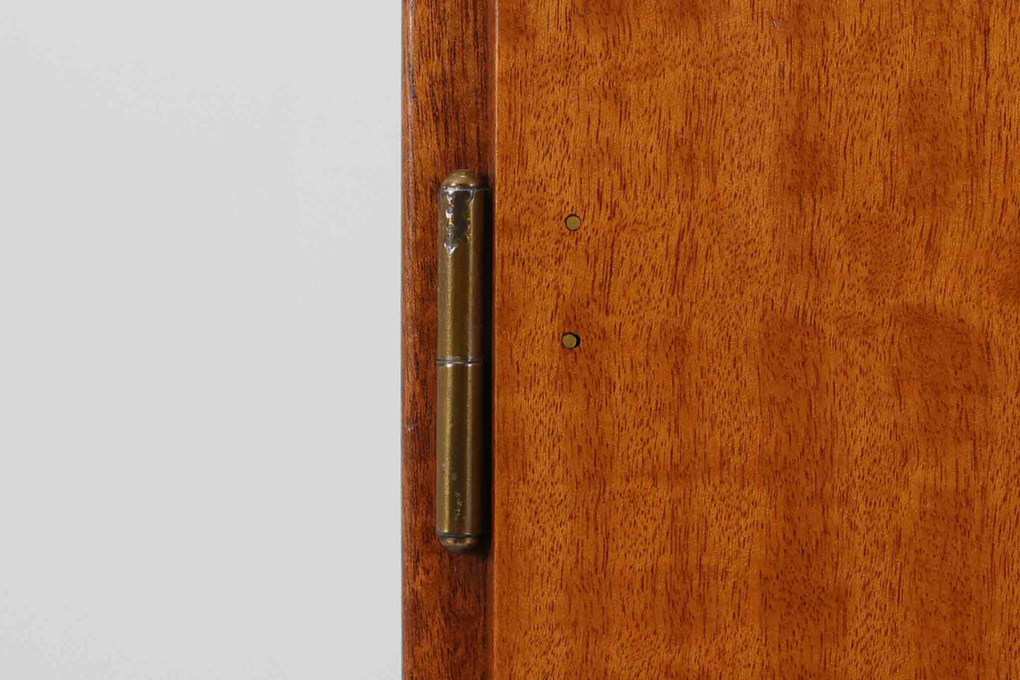 FDBモブラーでBorge mogensenの後任としてアートディレクターを務めたPoul m. Voltherによる、美しく洗練されたキャビネット。良質なマホガニー材の本体に、ビーチ材の脚部を組み合わせたコントラストが魅力です。真鍮の丸い鍵穴が特徴的な3枚の扉を備え、中央には調節可能な棚、両側には精巧な蟻継ぎが施された移動式の引き出しを配しています。下部には真鍮の俵型ハンドル付きの引き出しが3杯並び、細部へのこだわりが際立ちます。また、室内で靴を履く文化に配慮し、脚先には汚れ防止のための濃い塗装が施されています。1950年代にデザインされた本作は、先細りの脚やストレッチャーがミニマルな美しさを際立たせる一方、シンメトリーなフォルムや真鍮の装飾が伝統的なエレガンスを醸し出し、モダンとクラシックが調和した逸品です。