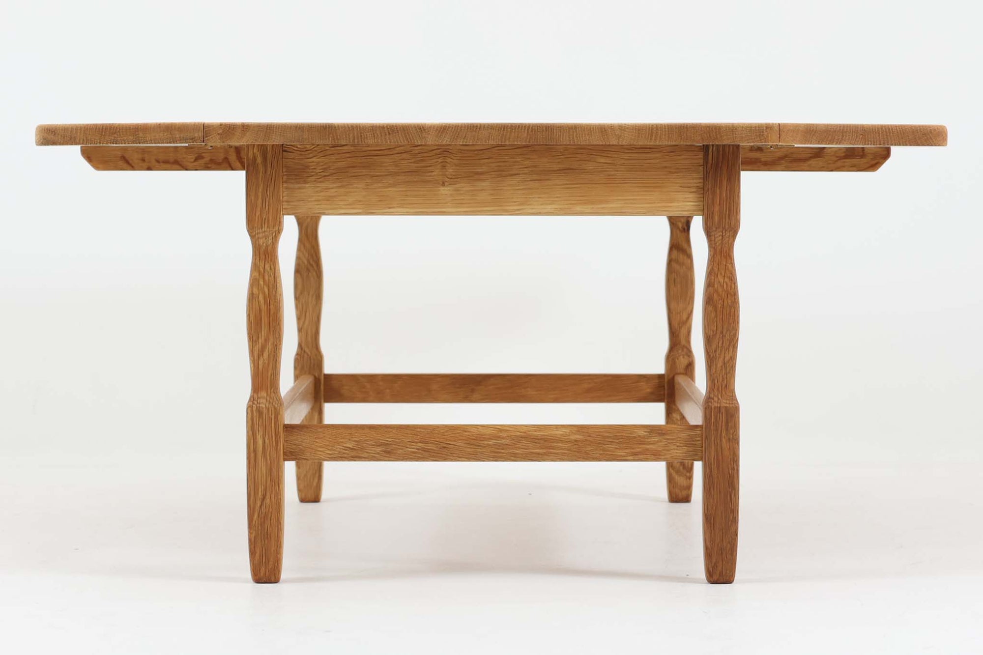 デンマークの建築家Henning Kjaernulf（ヘニング・ケアヌルフ）によってデザインされた、オーク無垢材のドロップリーフ式センターテーブルです。製造は高品質な家具で知られるEGモブラー社。無垢材ならではの美しい木目と、クラシカルで彫刻的な脚部のラインが印象的です。天板は両側に開閉式のリーフが備わっており、来客時や作業時には広げてスペースを拡張できるなど、実用性も兼ね備えています。テーブルの高さはやや高めの設計で、ソファ前に置いても手元が使いやすく、センターテーブルとして快適にお使いいただけます。必要に応じてサイドテーブルやティーテーブルとしても活躍する、用途の広い一台です。