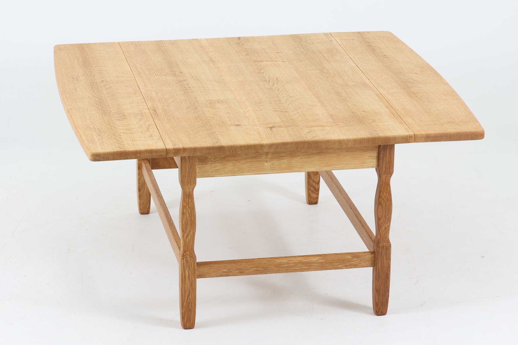 デンマークの建築家Henning Kjaernulf（ヘニング・ケアヌルフ）によってデザインされた、オーク無垢材のドロップリーフ式センターテーブルです。製造は高品質な家具で知られるEGモブラー社。無垢材ならではの美しい木目と、クラシカルで彫刻的な脚部のラインが印象的です。天板は両側に開閉式のリーフが備わっており、来客時や作業時には広げてスペースを拡張できるなど、実用性も兼ね備えています。テーブルの高さはやや高めの設計で、ソファ前に置いても手元が使いやすく、センターテーブルとして快適にお使いいただけます。必要に応じてサイドテーブルやティーテーブルとしても活躍する、用途の広い一台です。