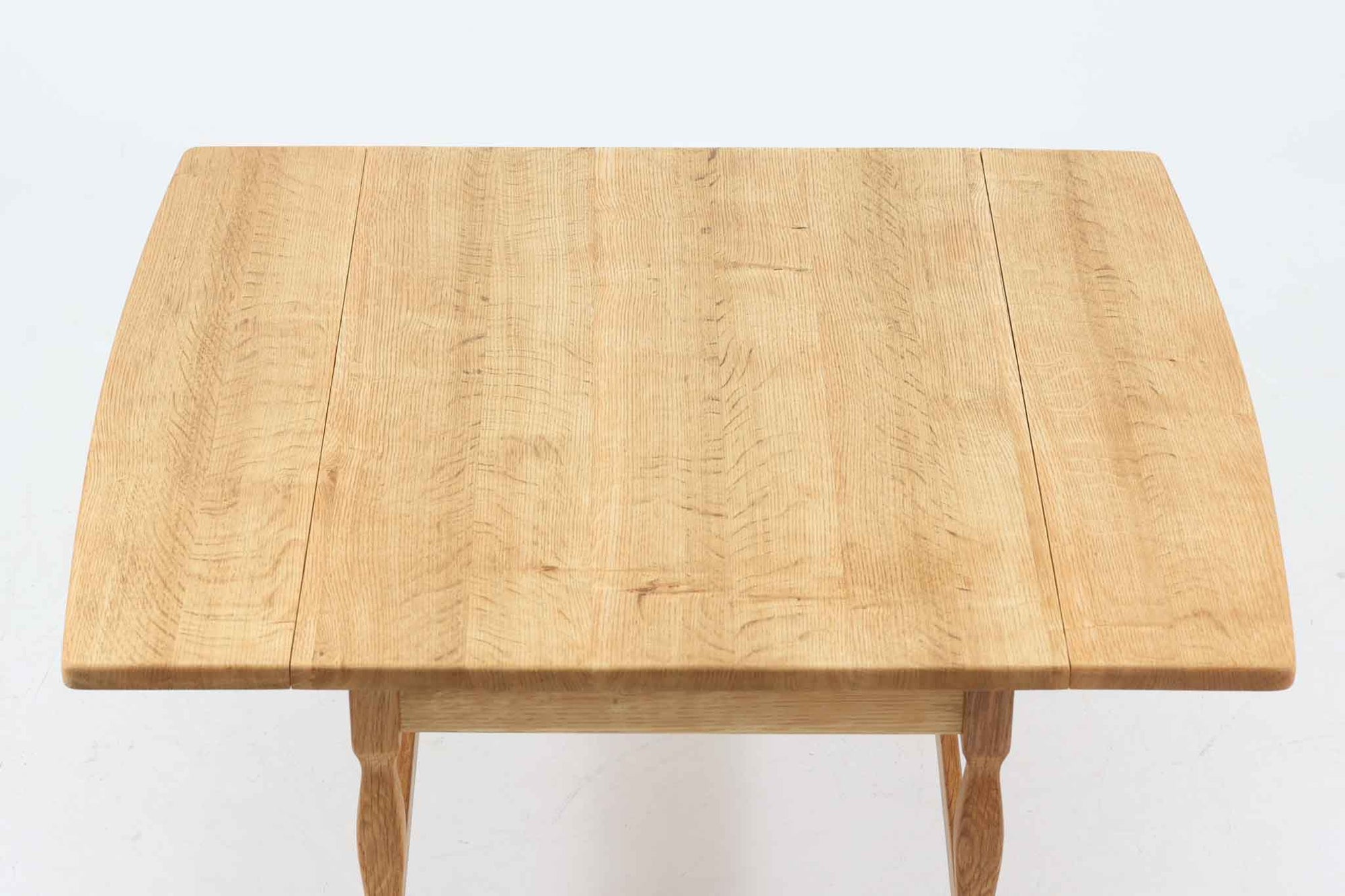 デンマークの建築家Henning Kjaernulf（ヘニング・ケアヌルフ）によってデザインされた、オーク無垢材のドロップリーフ式センターテーブルです。製造は高品質な家具で知られるEGモブラー社。無垢材ならではの美しい木目と、クラシカルで彫刻的な脚部のラインが印象的です。天板は両側に開閉式のリーフが備わっており、来客時や作業時には広げてスペースを拡張できるなど、実用性も兼ね備えています。テーブルの高さはやや高めの設計で、ソファ前に置いても手元が使いやすく、センターテーブルとして快適にお使いいただけます。必要に応じてサイドテーブルやティーテーブルとしても活躍する、用途の広い一台です。