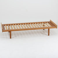 Ejvind A. Johanssonがデザインし、FDB Moblerが手掛けたベンチソファです。オーク材を使用したフレームは、経年により深みを増した木肌と美しい木目が魅力で、真鍮パーツがさりげないアクセントとして上品な存在感を添えています。すのこ状の座面や丸みを帯びた脚部、無駄を削ぎ落とした軽やかな構造には北欧デザインらしい機能美が感じられ、デイベッドやベンチとして空間に取り入れやすい一台。シンプルながら丁寧な木工技術が光る、希少性の高い北欧ビンテージ家具です。