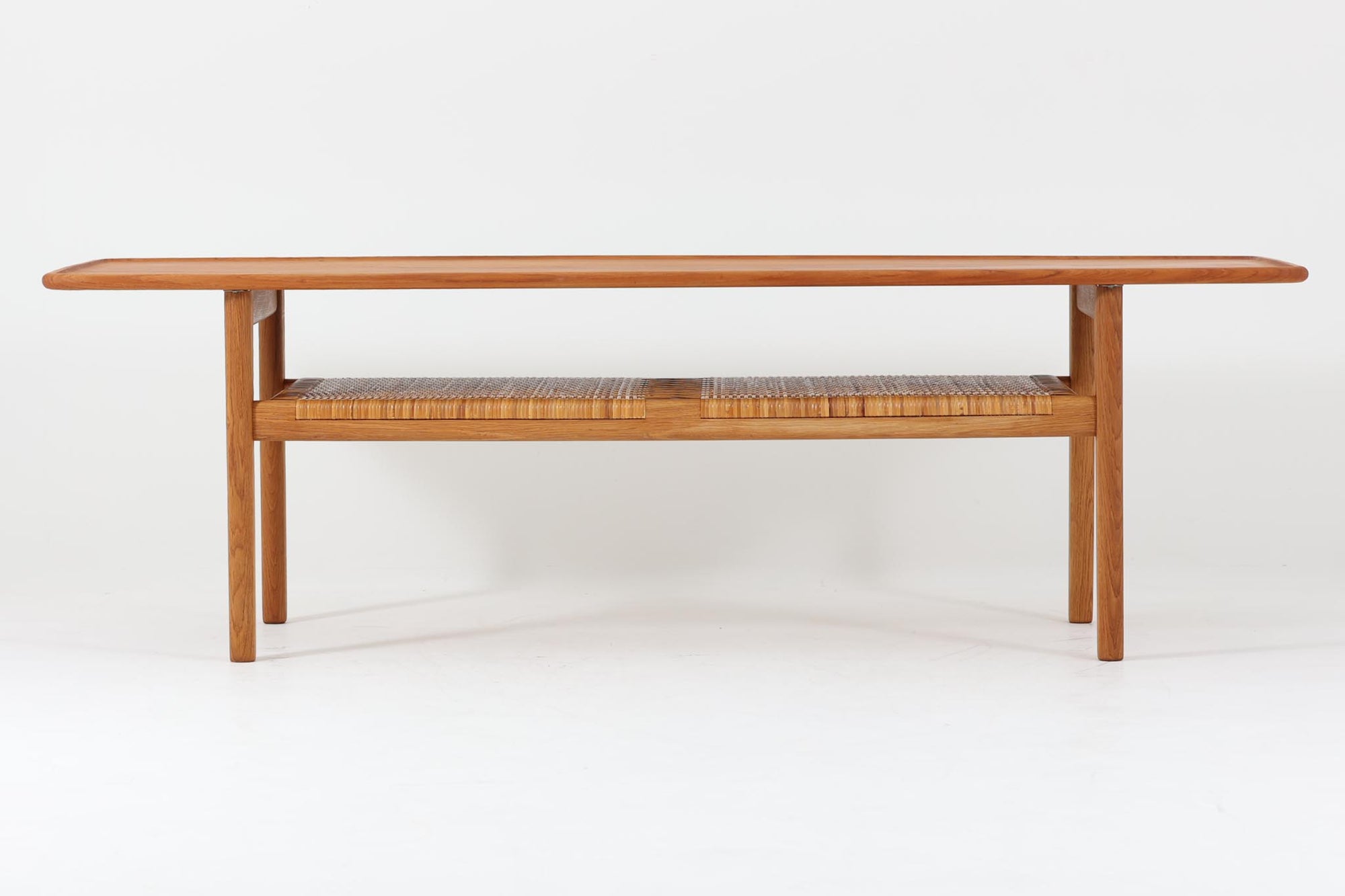 北欧より買い付けた、Hans J. WegnerによるAT10です。天板にはチーク無垢材が使われ、脚部にはオーク無垢材が採用されています。経年変化した籐の棚が特徴的で、温かみのある雰囲気を醸し出します。幅160cmというサイズ感は、3Pソファの前面に並べて使用すると、程良い距離感を保ちながら使いやすく、空間全体のバランスを整えます。縁が削り出されて丸みを帯びたデザインは、AT10の特徴であり、その独特の魅力が感じられます。