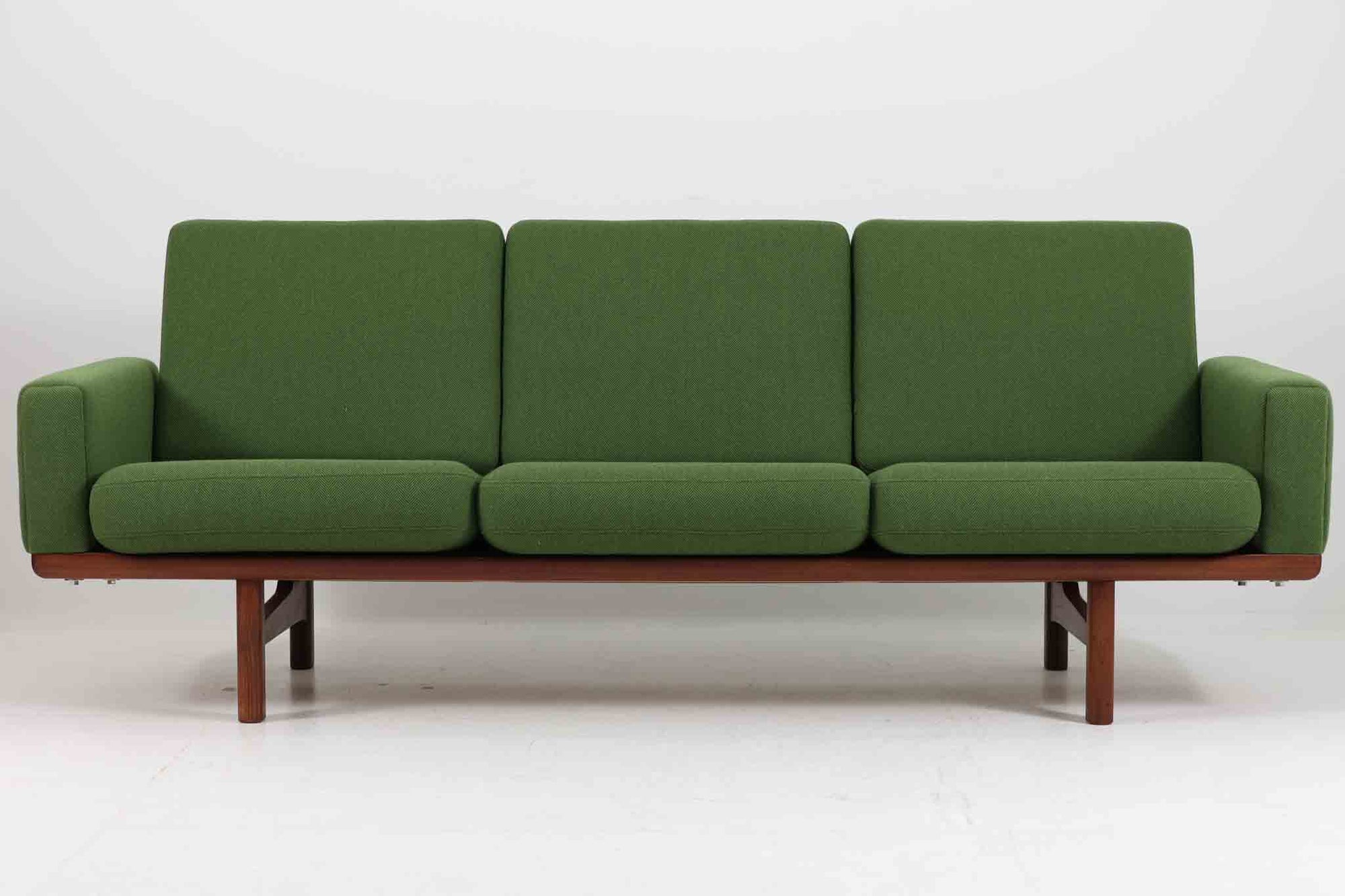 こちらは、ウェグナーデザインの人気モデル、GE236の3人掛けソファです。後ろ姿が非常に美しいため、あえて壁に寄せず背面を見せる配置もおすすめです。クッション内部にはスプリングが内蔵されており、座り心地も良好です。さらに、こちらは現地でも希少なチーク材（アフロモシア材）が使用された特別なモデルです。GETAmA社の刻印も確認できます。