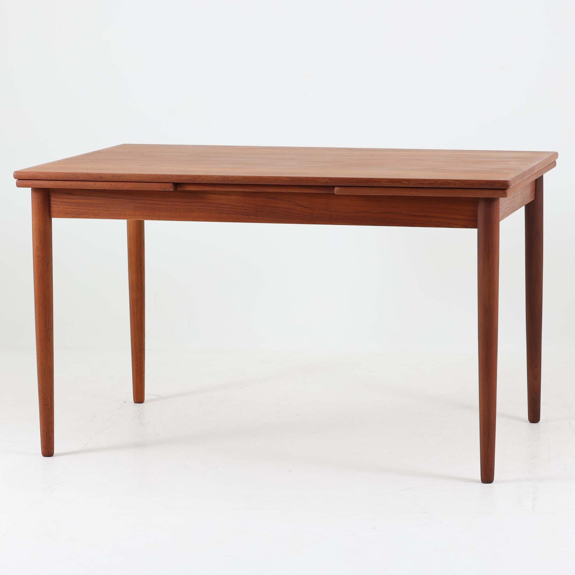 すっきりとした佇まいが魅力のこちらのエクステンションダイニングテーブルは、チーク材特有の深みある色合いと木目の美しさが際立つ北欧ビンテージ品で、天板下に格納された拡張板を引き出すことで幅124cmから207cmまで伸長可能な実用性に優れた一台です。シンプルで洗練されたフォルムとテーパードレッグのバランスが絶妙で、ダイニングシーンに温もりと上質さを添えます。デザイナー不明ながら、当時の丁寧な造りと素材選びにより、経年とともに増す風合いもお楽しみいただけます。