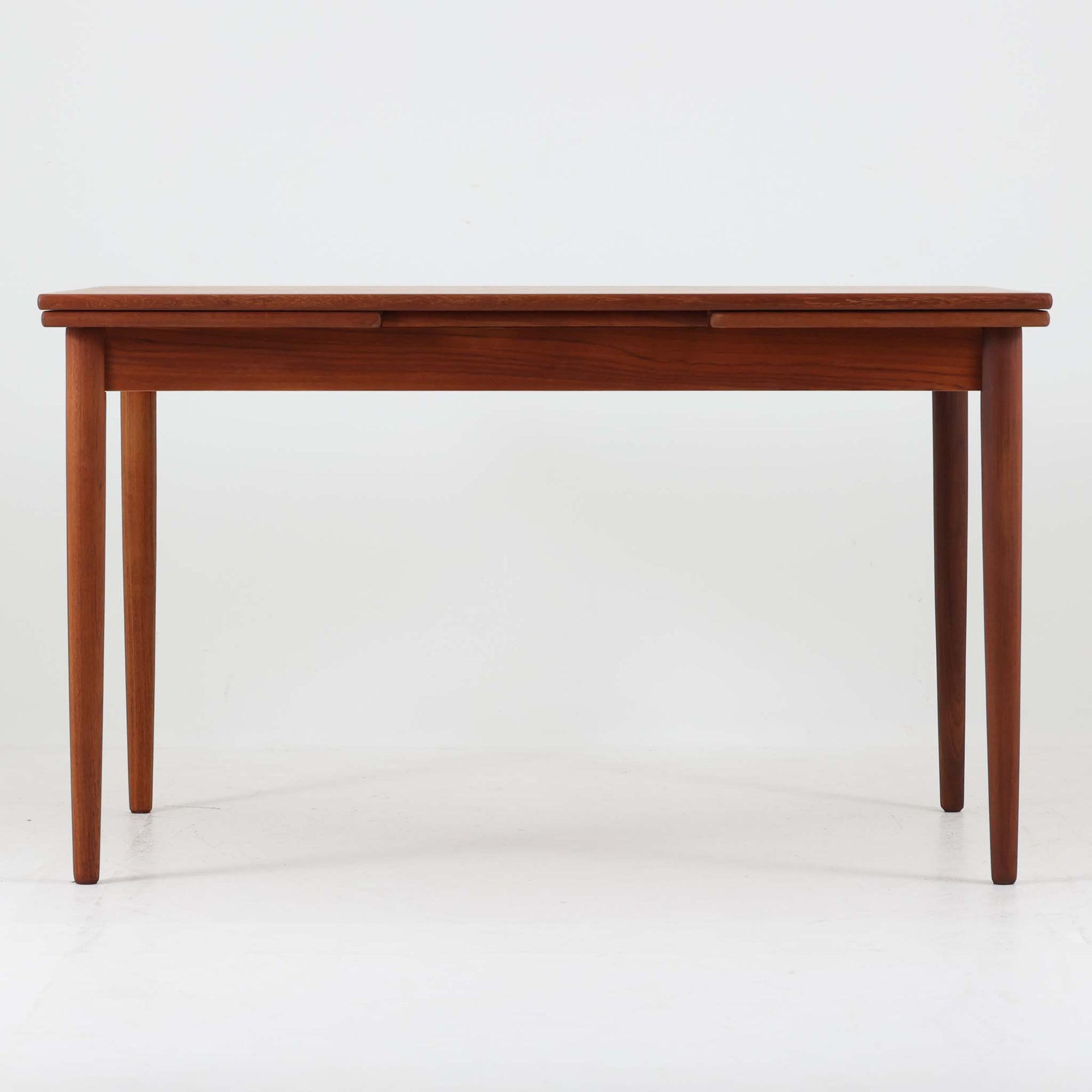 すっきりとした佇まいが魅力のこちらのエクステンションダイニングテーブルは、チーク材特有の深みある色合いと木目の美しさが際立つ北欧ビンテージ品で、天板下に格納された拡張板を引き出すことで幅124cmから207cmまで伸長可能な実用性に優れた一台です。シンプルで洗練されたフォルムとテーパードレッグのバランスが絶妙で、ダイニングシーンに温もりと上質さを添えます。デザイナー不明ながら、当時の丁寧な造りと素材選びにより、経年とともに増す風合いもお楽しみいただけます。