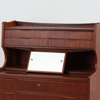 デンマーク製のチーク材によるライティングビューロです。幅85cmと程よいサイズ感で、上段には小引き出しを備え、小物や文具を整理しやすい構造になっています。中央のライティング天板は手前にスライドさせることで作業スペースが確保でき、書き物やノートPCの使用に最適です。さらに、内部には鏡が備わっており、ドレッサーとしても活用できる実用的なデザインです。下段には容量の大きな引き出しが3杯あり、衣類や書類の収納にも対応します。チーク材特有の温かみのある木目と経年による艶が味わい深く、実用性と美観を兼ね備えたビンテージ家具です。