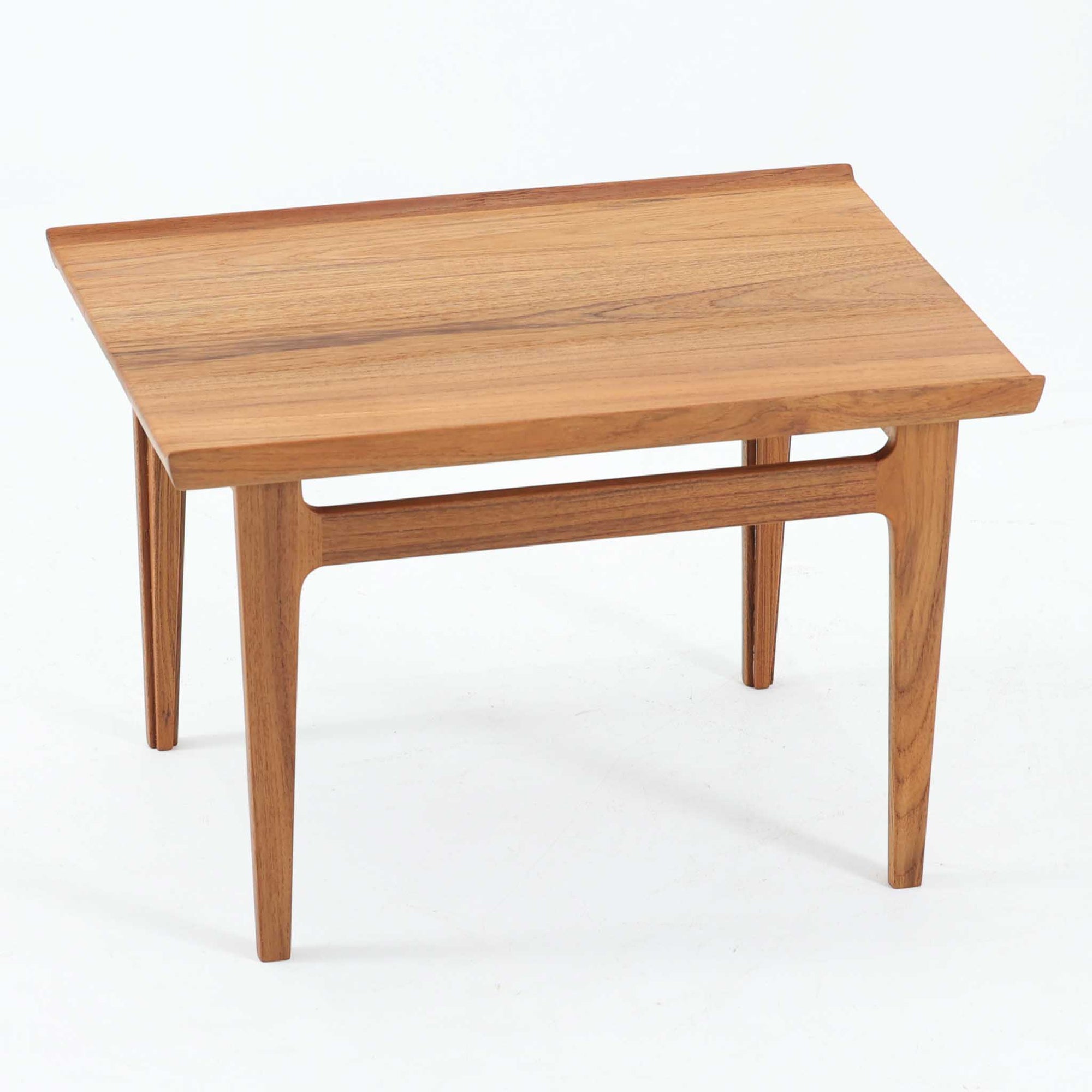 デンマークの巨匠フィン・ユールによるデザイン、France &amp; Son社製のサイドテーブル「FD635」です。ロゴより1957年頃に製造されたと推測される本品は、チーク無垢材を贅沢に使用し、滑らかな脚部の曲線と柔らかなエッジラインが見事に調和した美しいデザインが魅力です。天板の縁にはわずかな立ち上がりが設けられ、機能性と造形美を兼ね備えた構造となっています。彫刻的ともいえる有機的なフォルムはフィン・ユールの真骨頂であり、リビングやベッドサイドで北欧家具の上質な存在感を引き立てる逸品です。