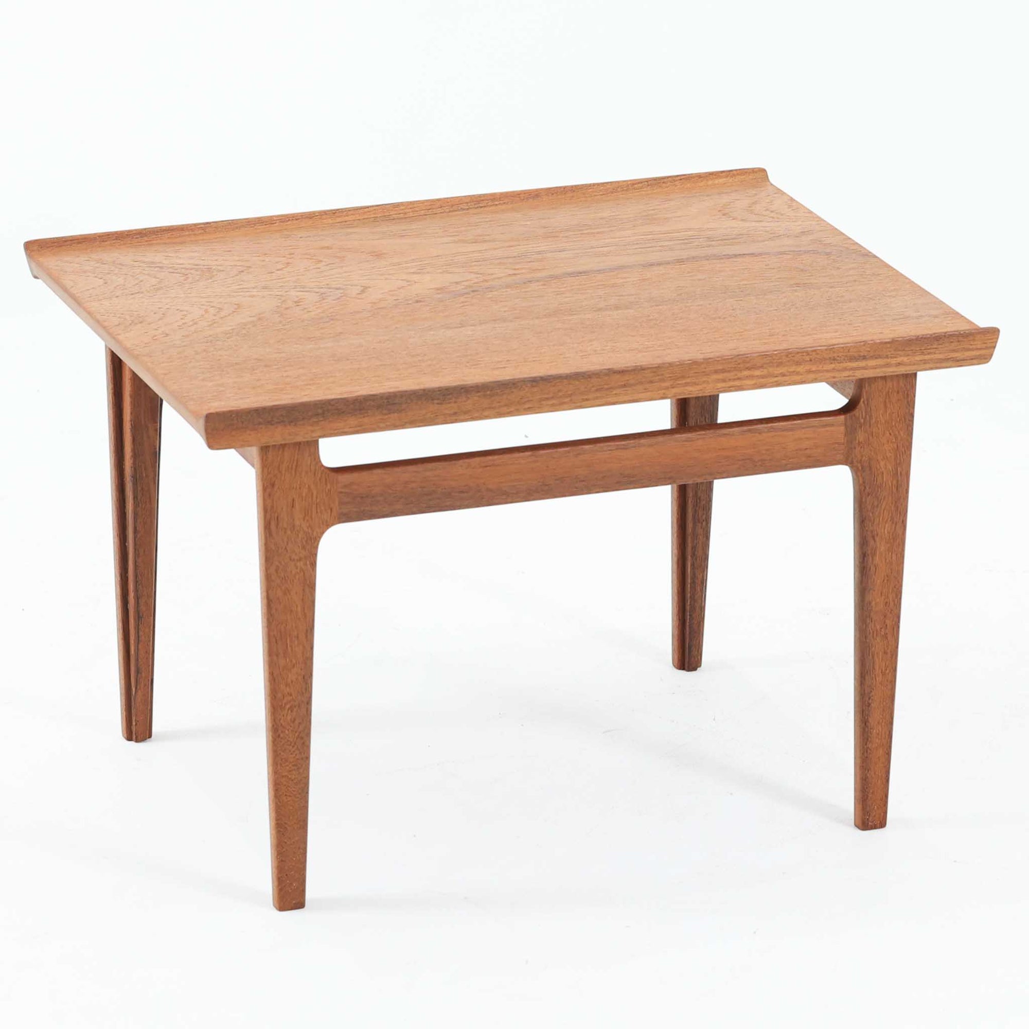 デンマークの巨匠フィン・ユールによるデザイン、France &amp; Son社製のサイドテーブル「FD635」です。ロゴより1957年頃に製造されたと推測される本品は、チーク無垢材を贅沢に使用し、滑らかな脚部の曲線と柔らかなエッジラインが見事に調和した美しいデザインが魅力です。天板の縁にはわずかな立ち上がりが設けられ、機能性と造形美を兼ね備えた構造となっています。彫刻的ともいえる有機的なフォルムはフィン・ユールの真骨頂であり、リビングやベッドサイドで北欧家具の上質な存在感を引き立てる逸品です。