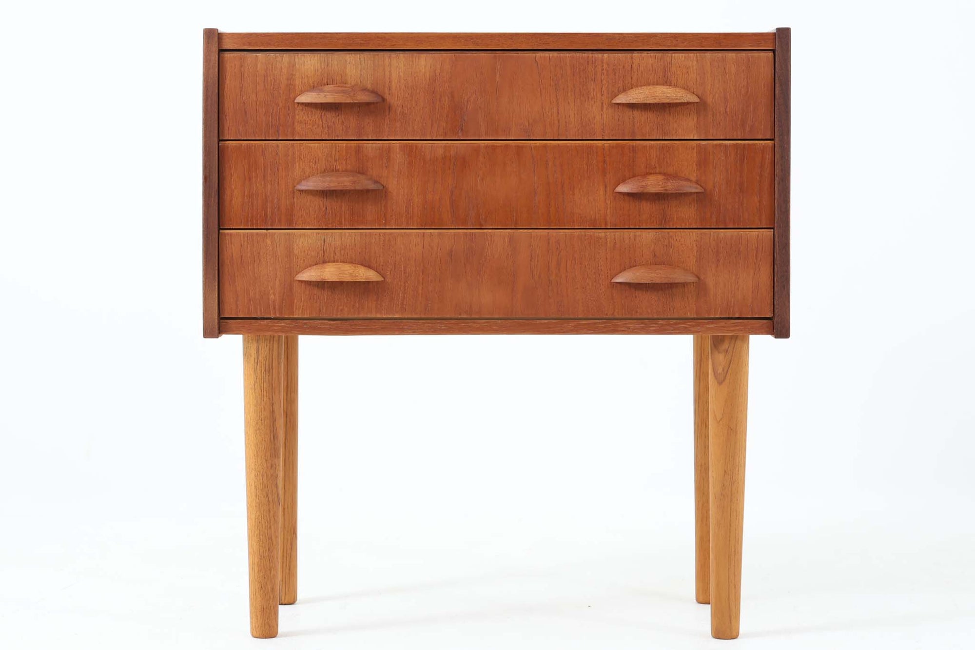 温かみのあるチーク材を用いた、デンマーク製のビンテージ3段チェストです。美しい木目と落ち着いた色合いが魅力で、引き出しには半月型の木製ハンドルがあしらわれています。直線的でシンプルなフォルムに、丸みを帯びたチーク材の脚が調和し、全体として統一感のある佇まいに仕上がっています。元の脚部に破損が見られたため、同じくチーク材で新たに作成しております。リビングや寝室、玄関など幅広い空間でお使いいただける実用的な収納家具です。