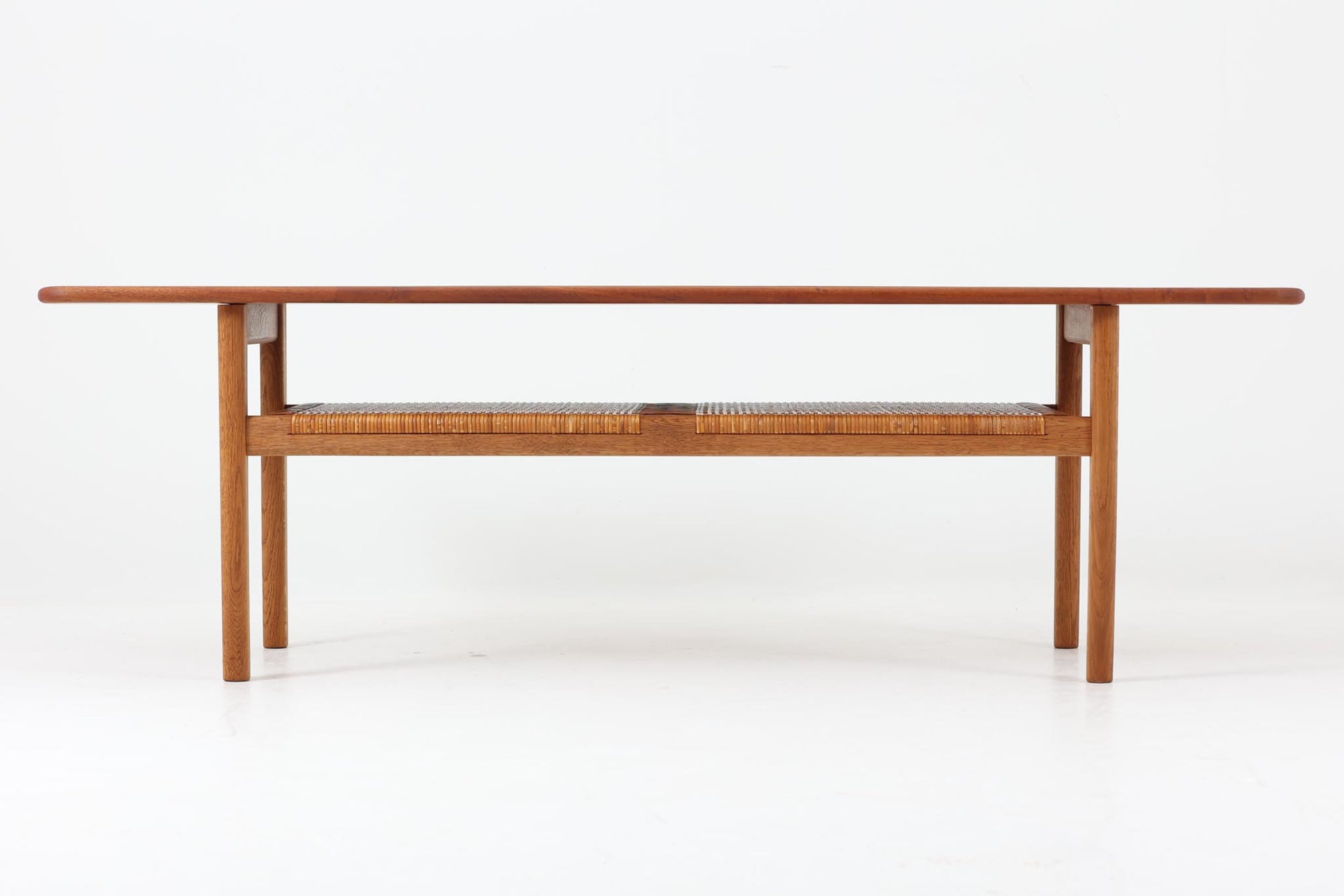 北欧より買い付けた、Hans J. WegnerによるAT10です。天板にはチーク無垢材が使われ、脚部にはオーク無垢材が採用されています。経年変化した籐の棚が特徴的で、温かみのある雰囲気を醸し出します。幅160cmというサイズ感は、3Pソファの前面に並べて使用すると、程良い距離感を保ちながら使いやすく、空間全体のバランスを整えます。縁が削り出されて丸みを帯びたデザインは、AT10の特徴であり、その独特の魅力が感じられます。天板裏面にはAndreas Tuck社の刻印がございます。