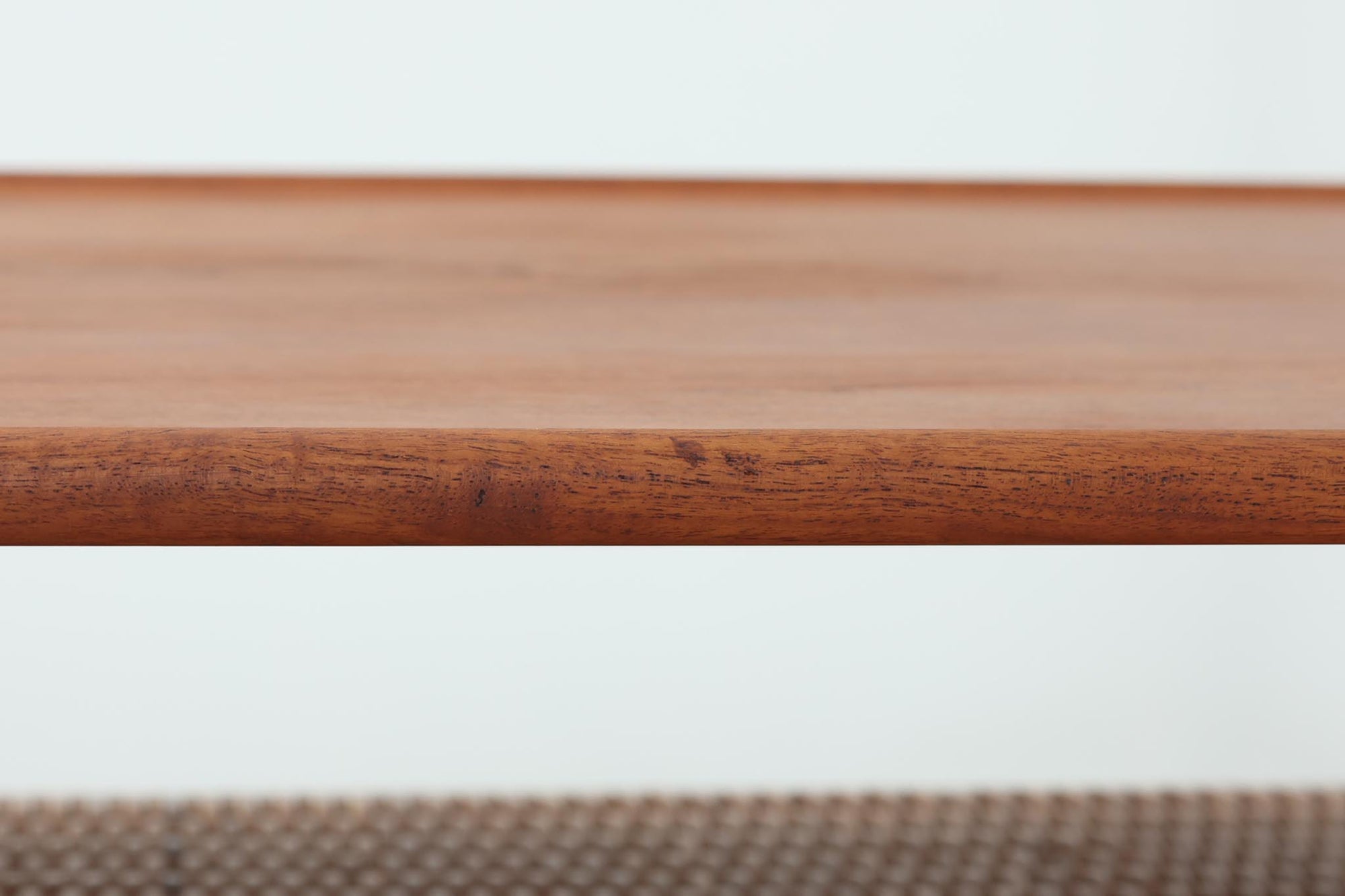 北欧より買い付けた、Hans J. WegnerによるAT10です。天板にはチーク無垢材が使われ、脚部にはオーク無垢材が採用されています。経年変化した籐の棚が特徴的で、温かみのある雰囲気を醸し出します。幅160cmというサイズ感は、3Pソファの前面に並べて使用すると、程良い距離感を保ちながら使いやすく、空間全体のバランスを整えます。縁が削り出されて丸みを帯びたデザインは、AT10の特徴であり、その独特の魅力が感じられます。天板裏面にはAndreas Tuck社の刻印がございます。