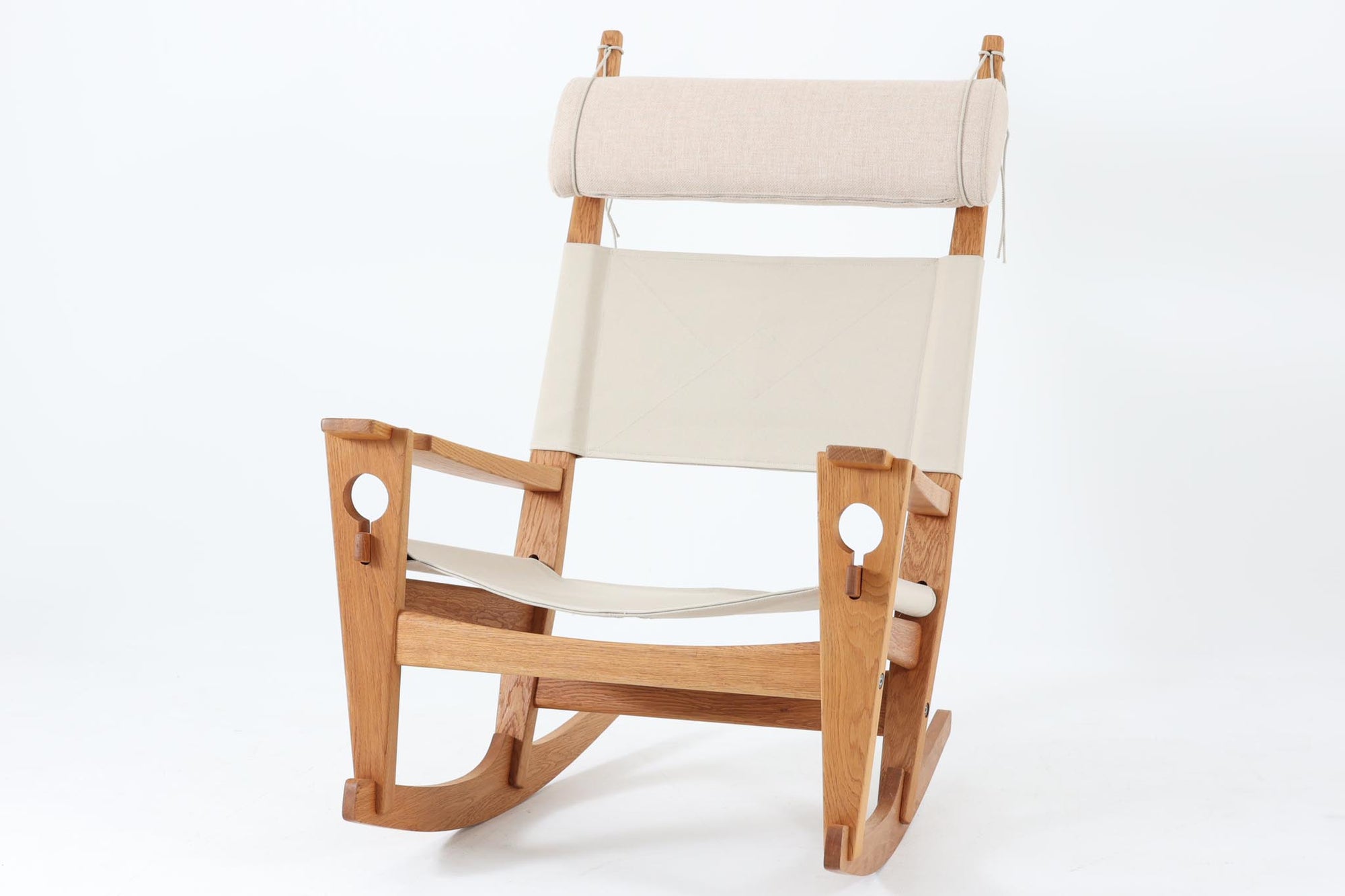 Hans J. Wegnerが1967年にデザインしたロッキングチェア「キーホールチェア（GE673）」は、GETAmA社製の一脚です。特徴的な「鍵穴」のような形状の座面固定方法が名前の由来で、左右のアーム下に引っ掛けた2本の棒が座面を支える構造です。帆布製の背もたれと座面は、ハンモックのような座り心地を提供し、まるで包み込まれるような安心感を感じさせます。ロッキングチェアならではの揺れと、程よい可動領域が特徴で、家の中でゆったりとくつろぐのに最適です。座面は簡単に取り外せ、クリーニングにも配慮されています。軽量で機能性とデザインが見事に調和した、ウェグナーならではの作品です。