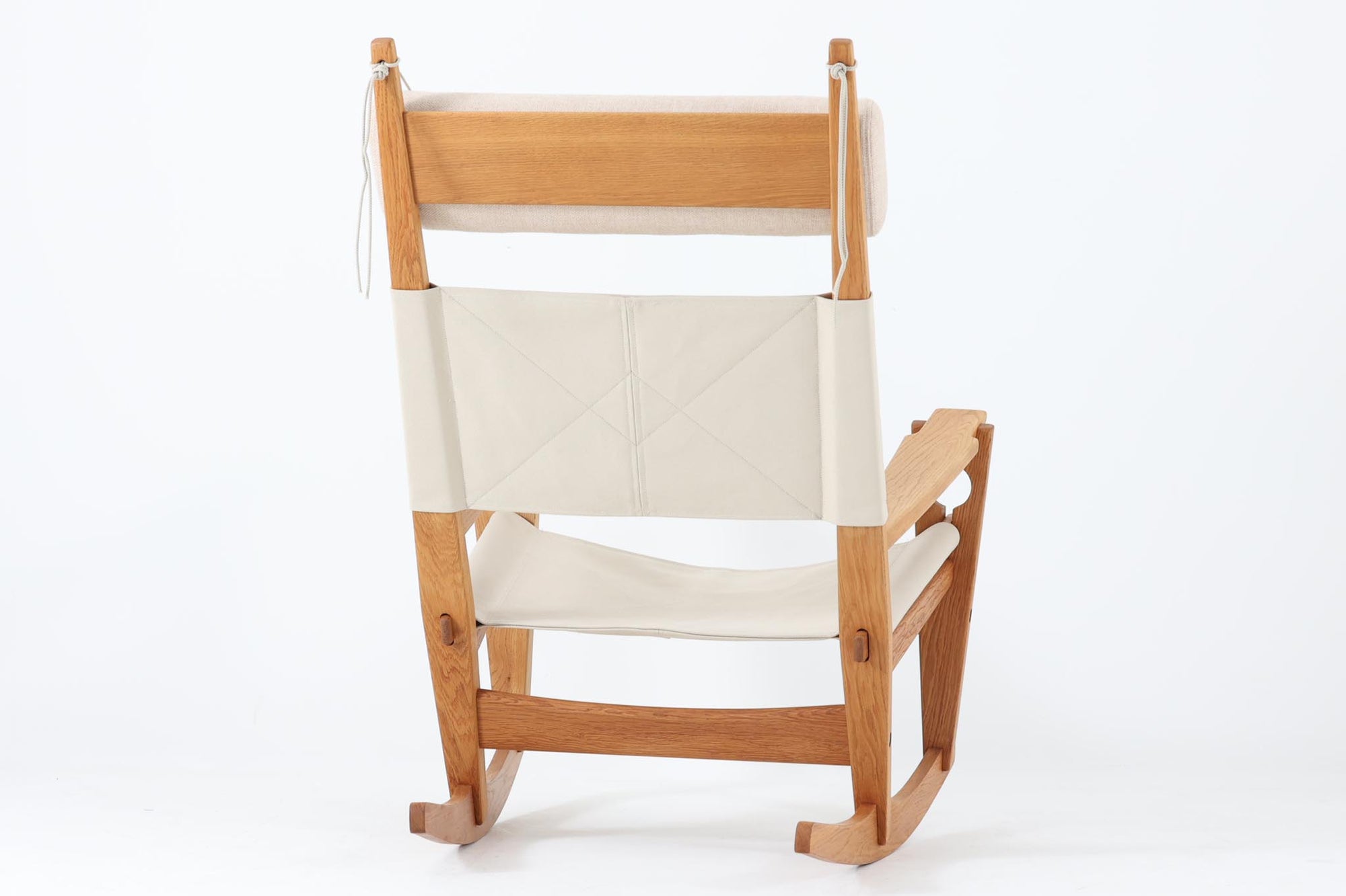 Hans J. Wegnerが1967年にデザインしたロッキングチェア「キーホールチェア（GE673）」は、GETAmA社製の一脚です。特徴的な「鍵穴」のような形状の座面固定方法が名前の由来で、左右のアーム下に引っ掛けた2本の棒が座面を支える構造です。帆布製の背もたれと座面は、ハンモックのような座り心地を提供し、まるで包み込まれるような安心感を感じさせます。ロッキングチェアならではの揺れと、程よい可動領域が特徴で、家の中でゆったりとくつろぐのに最適です。座面は簡単に取り外せ、クリーニングにも配慮されています。軽量で機能性とデザインが見事に調和した、ウェグナーならではの作品です。