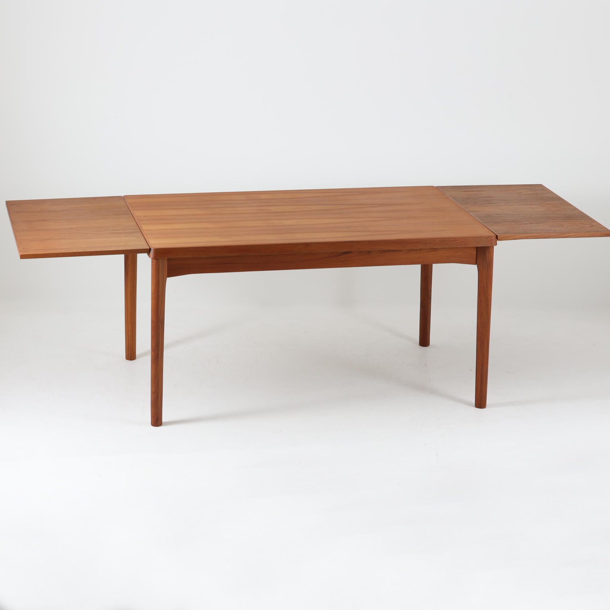 Henning Kjaernulf（ヘニング・ケアヌルフ）によってデザインされ、Vejle Stole og Mobelfabrik社が製造したデンマーク製のエクステンションダイニングテーブル。温もりあるチーク材と美しく面取りされたエッジラインが特徴です。両端のリーフを引き出すだけで最大239cmまで拡張でき、日常使いから来客時まで柔軟に対応。脚部はすっきりとした削り出しのディテールが施され、軽やかさと安定感を両立しています。素材の上質さと機能美を兼ね備えた、北欧ビンテージ家具の魅力あふれる一台です。