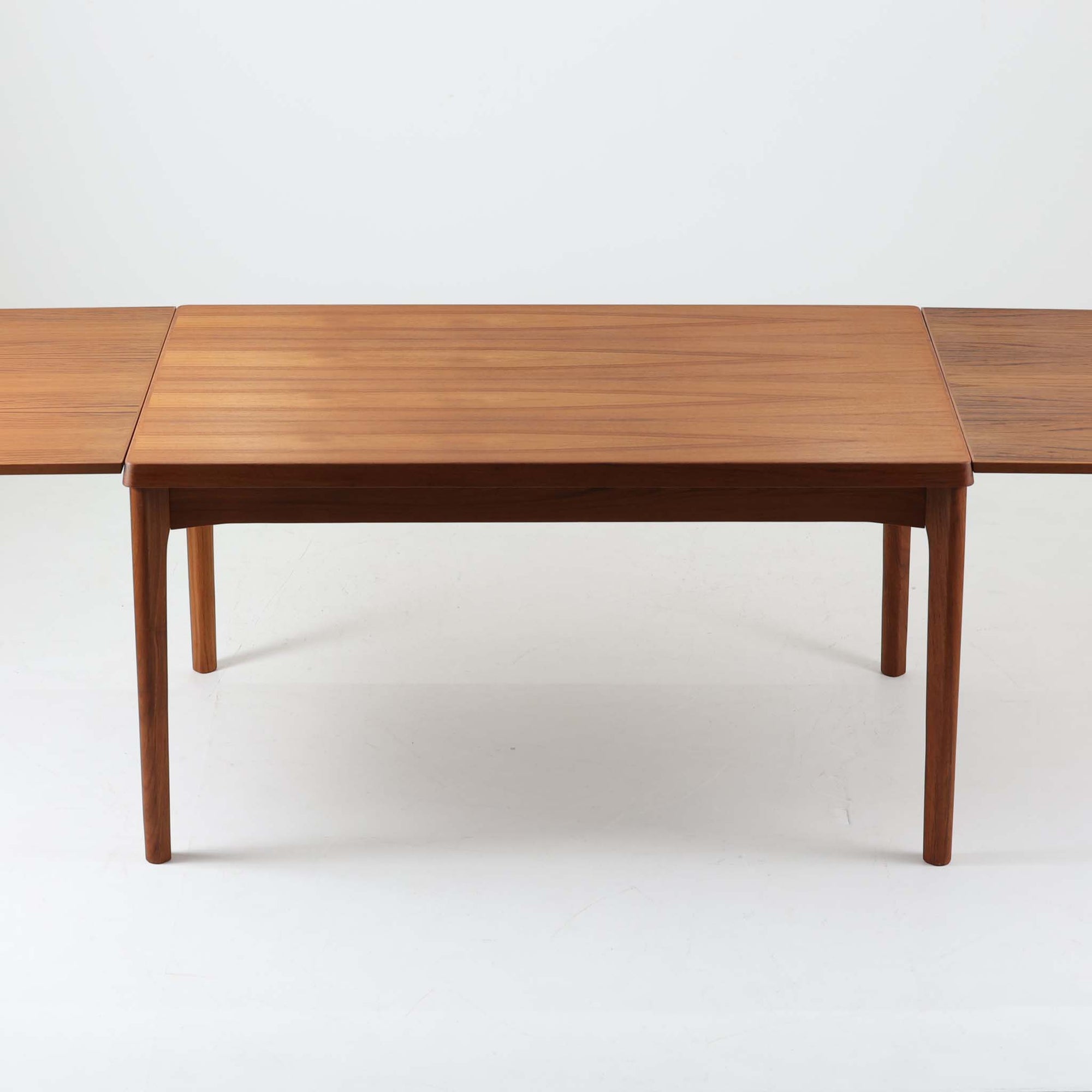 Henning Kjaernulf（ヘニング・ケアヌルフ）によってデザインされ、Vejle Stole og Mobelfabrik社が製造したデンマーク製のエクステンションダイニングテーブル。温もりあるチーク材と美しく面取りされたエッジラインが特徴です。両端のリーフを引き出すだけで最大239cmまで拡張でき、日常使いから来客時まで柔軟に対応。脚部はすっきりとした削り出しのディテールが施され、軽やかさと安定感を両立しています。素材の上質さと機能美を兼ね備えた、北欧ビンテージ家具の魅力あふれる一台です。