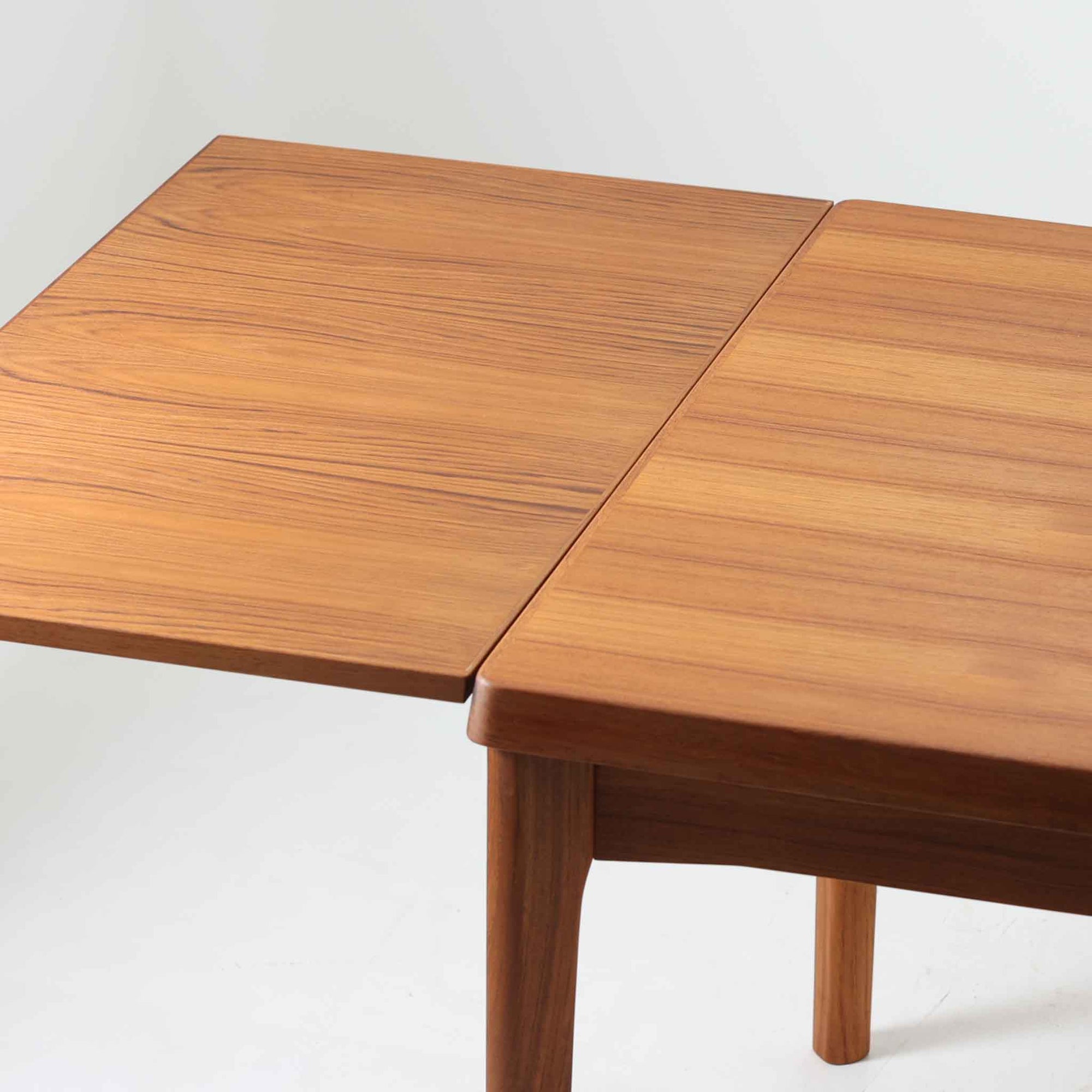 Henning Kjaernulf（ヘニング・ケアヌルフ）によってデザインされ、Vejle Stole og Mobelfabrik社が製造したデンマーク製のエクステンションダイニングテーブル。温もりあるチーク材と美しく面取りされたエッジラインが特徴です。両端のリーフを引き出すだけで最大239cmまで拡張でき、日常使いから来客時まで柔軟に対応。脚部はすっきりとした削り出しのディテールが施され、軽やかさと安定感を両立しています。素材の上質さと機能美を兼ね備えた、北欧ビンテージ家具の魅力あふれる一台です。