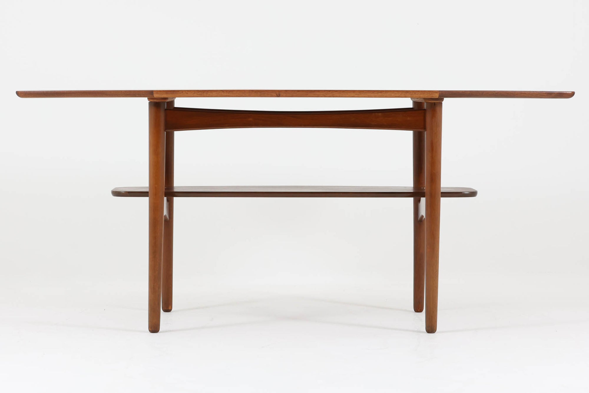 台形を基にした多角形の天板が特徴的な、美しいビンテージのセンターテーブル。心地よい木目が際立つウォールナット材の天板と、ナチュラルな風合いのビーチ材の組み合わせが、温かみのある佇まいを演出しています。天板と脚部、棚板の接続部には丸い真鍮があしらわれ、シンプルなフォルムの中に洗練されたアクセントを加えています。また、脚部をつなぐ幕板の形状も独特で、細部にまでこだわりが感じられるデザインです。デザイナーは不明ですが、細部の仕上げや素材選びから高いクオリティがうかがえる一品。モダンとクラシックが絶妙に調和した、上質なビンテージテーブルです。