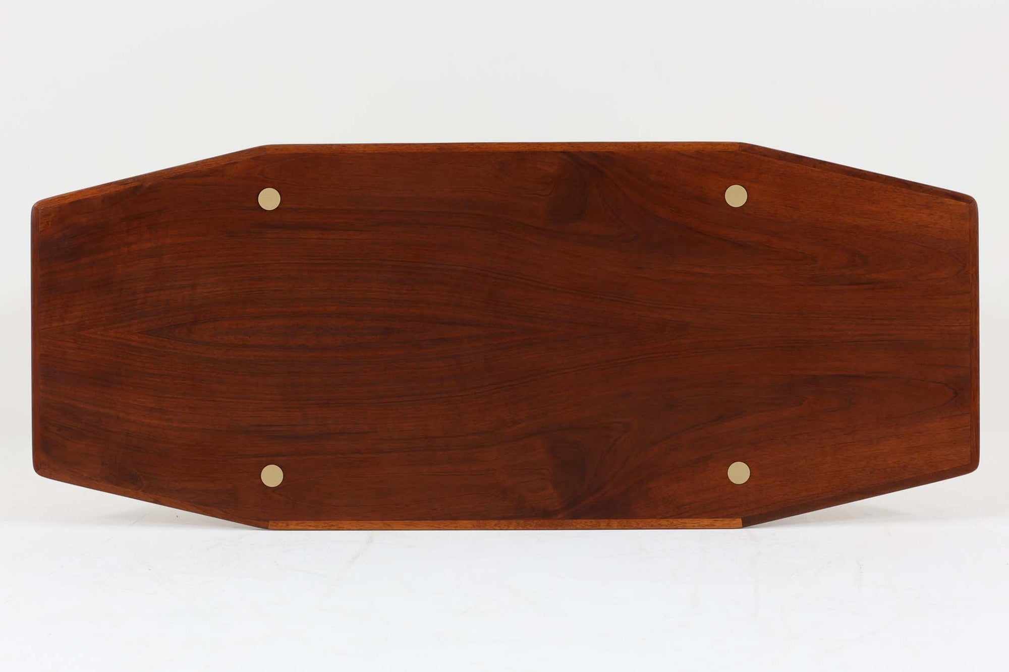 台形を基にした多角形の天板が特徴的な、美しいビンテージのセンターテーブル。心地よい木目が際立つウォールナット材の天板と、ナチュラルな風合いのビーチ材の組み合わせが、温かみのある佇まいを演出しています。天板と脚部、棚板の接続部には丸い真鍮があしらわれ、シンプルなフォルムの中に洗練されたアクセントを加えています。また、脚部をつなぐ幕板の形状も独特で、細部にまでこだわりが感じられるデザインです。デザイナーは不明ですが、細部の仕上げや素材選びから高いクオリティがうかがえる一品。モダンとクラシックが絶妙に調和した、上質なビンテージテーブルです。