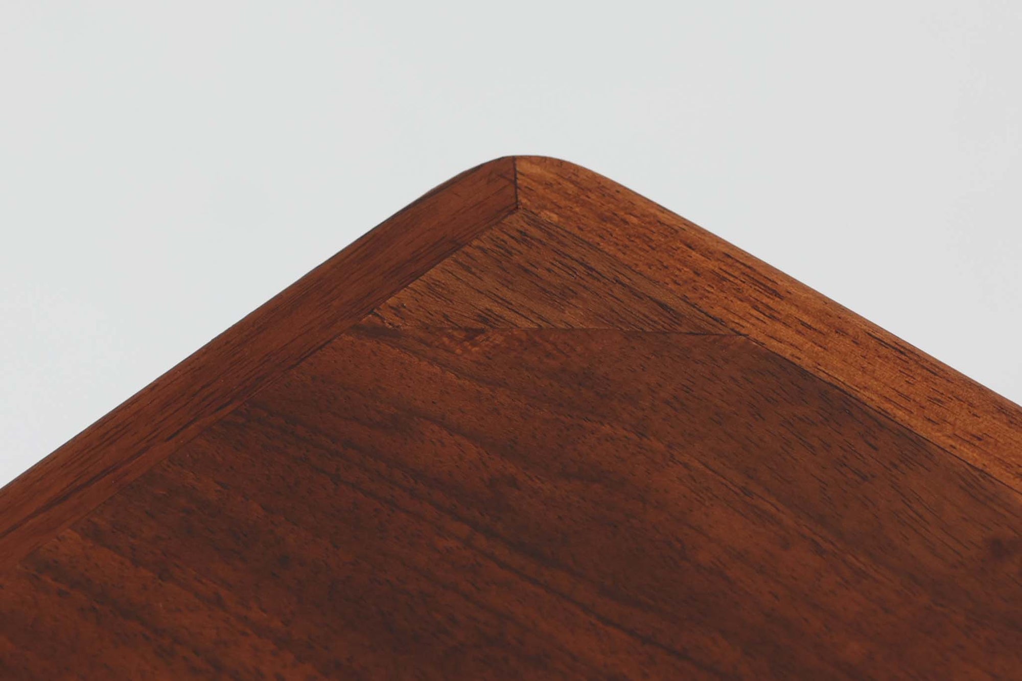 台形を基にした多角形の天板が特徴的な、美しいビンテージのセンターテーブル。心地よい木目が際立つウォールナット材の天板と、ナチュラルな風合いのビーチ材の組み合わせが、温かみのある佇まいを演出しています。天板と脚部、棚板の接続部には丸い真鍮があしらわれ、シンプルなフォルムの中に洗練されたアクセントを加えています。また、脚部をつなぐ幕板の形状も独特で、細部にまでこだわりが感じられるデザインです。デザイナーは不明ですが、細部の仕上げや素材選びから高いクオリティがうかがえる一品。モダンとクラシックが絶妙に調和した、上質なビンテージテーブルです。