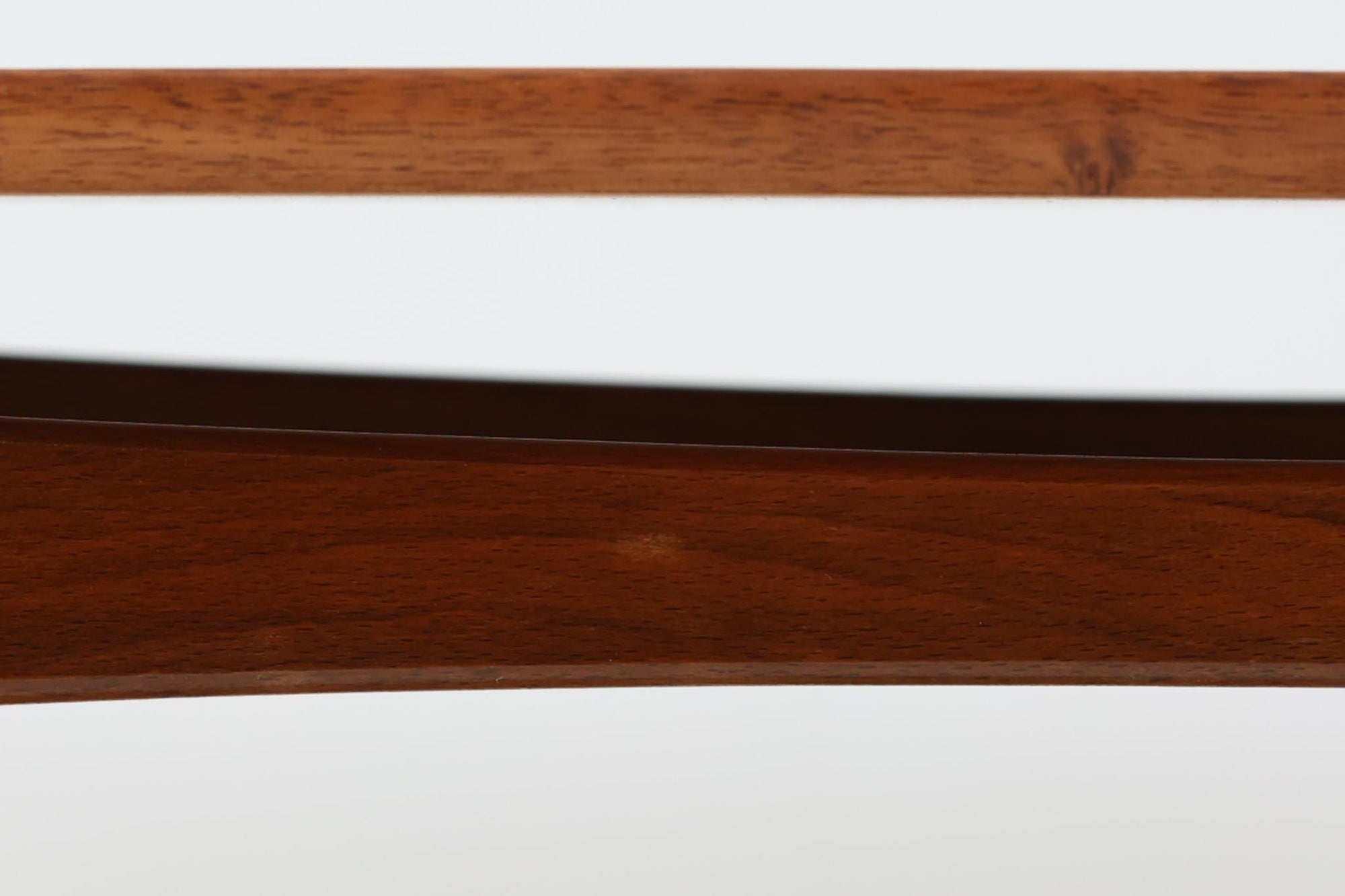 台形を基にした多角形の天板が特徴的な、美しいビンテージのセンターテーブル。心地よい木目が際立つウォールナット材の天板と、ナチュラルな風合いのビーチ材の組み合わせが、温かみのある佇まいを演出しています。天板と脚部、棚板の接続部には丸い真鍮があしらわれ、シンプルなフォルムの中に洗練されたアクセントを加えています。また、脚部をつなぐ幕板の形状も独特で、細部にまでこだわりが感じられるデザインです。デザイナーは不明ですが、細部の仕上げや素材選びから高いクオリティがうかがえる一品。モダンとクラシックが絶妙に調和した、上質なビンテージテーブルです。