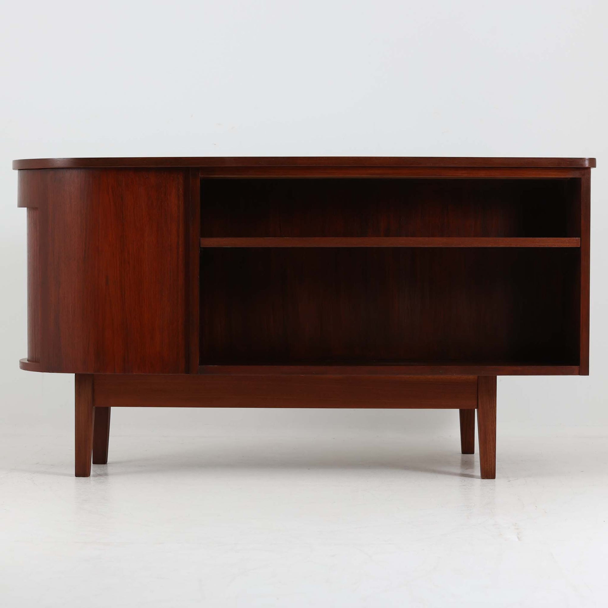 デンマーク製キドニーデスクです。緩やかな曲線を描く天板と、右側に配された蛇腹扉収納が特徴的な美しいデザインで、北欧モダンの洗練された造形美が感じられます。上質なチーク材が用いられ、深みのある色合いと木目が経年により一層味わいを増しています。背面にも収納棚を備えており、空間の中央に置いても様になる造りです。書斎デスクとしてはもちろん、ショップのカウンターや作業台としても活躍する存在感のある一台です。