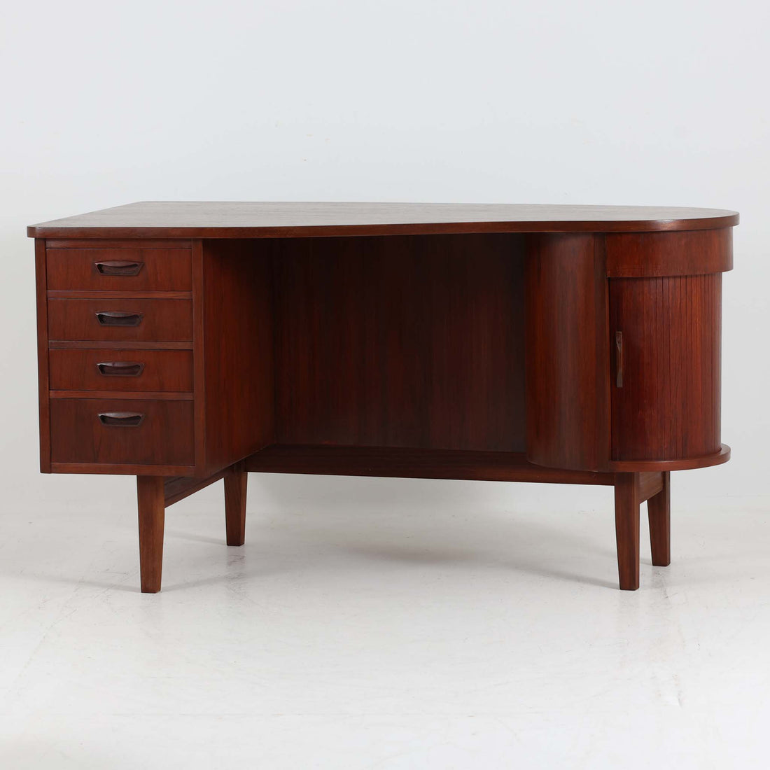 デンマーク製キドニーデスクです。緩やかな曲線を描く天板と、右側に配された蛇腹扉収納が特徴的な美しいデザインで、北欧モダンの洗練された造形美が感じられます。上質なチーク材が用いられ、深みのある色合いと木目が経年により一層味わいを増しています。背面にも収納棚を備えており、空間の中央に置いても様になる造りです。書斎デスクとしてはもちろん、ショップのカウンターや作業台としても活躍する存在感のある一台です。