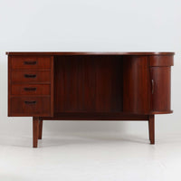 デンマーク製キドニーデスクです。緩やかな曲線を描く天板と、右側に配された蛇腹扉収納が特徴的な美しいデザインで、北欧モダンの洗練された造形美が感じられます。上質なチーク材が用いられ、深みのある色合いと木目が経年により一層味わいを増しています。背面にも収納棚を備えており、空間の中央に置いても様になる造りです。書斎デスクとしてはもちろん、ショップのカウンターや作業台としても活躍する存在感のある一台です。