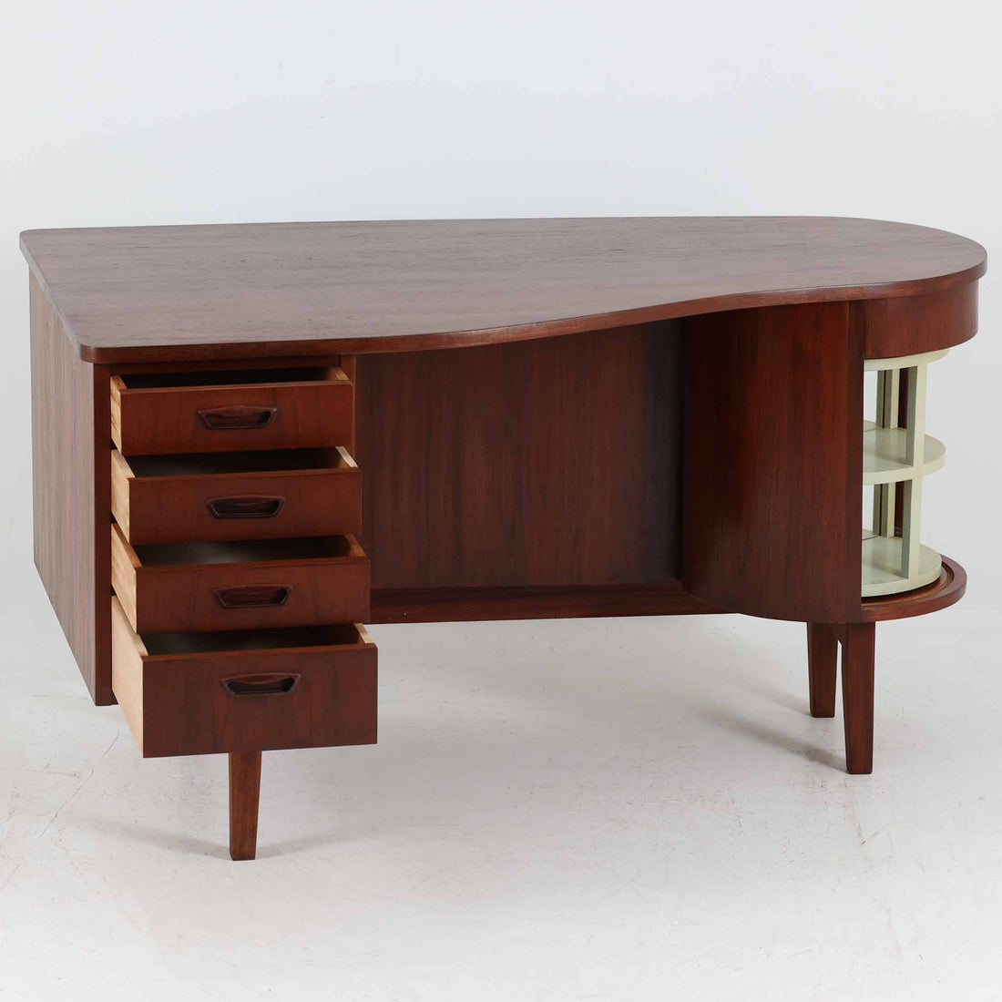 デンマーク製キドニーデスクです。緩やかな曲線を描く天板と、右側に配された蛇腹扉収納が特徴的な美しいデザインで、北欧モダンの洗練された造形美が感じられます。上質なチーク材が用いられ、深みのある色合いと木目が経年により一層味わいを増しています。背面にも収納棚を備えており、空間の中央に置いても様になる造りです。書斎デスクとしてはもちろん、ショップのカウンターや作業台としても活躍する存在感のある一台です。