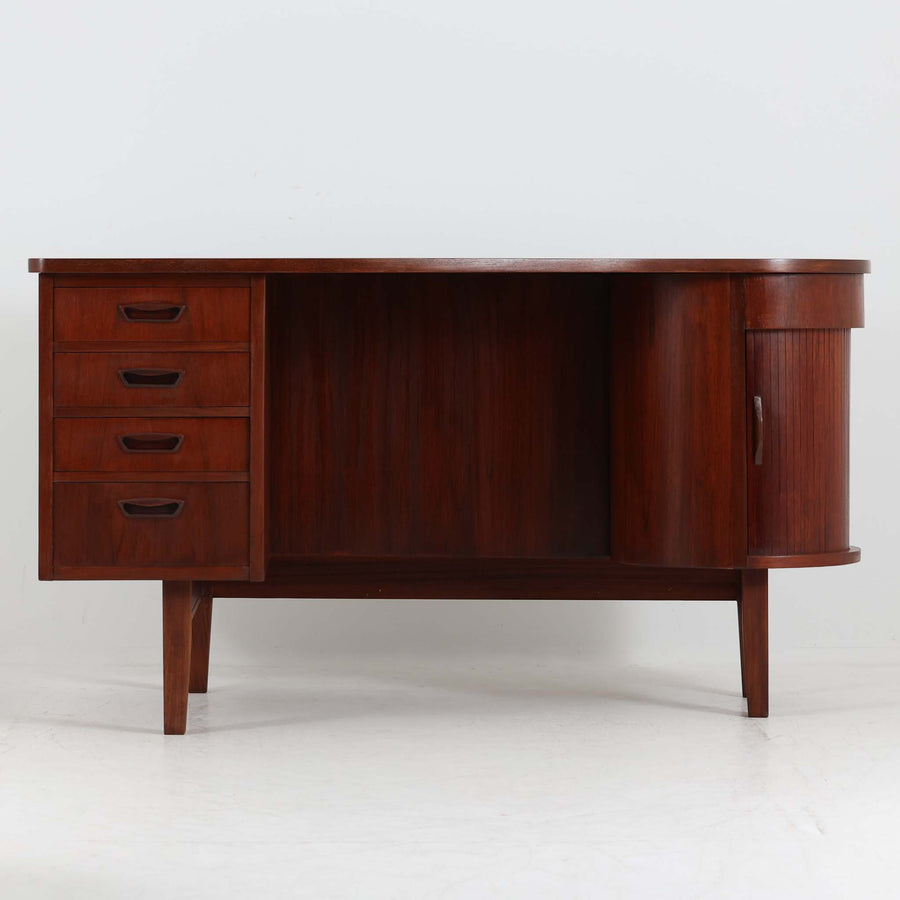 デンマーク製キドニーデスクです。緩やかな曲線を描く天板と、右側に配された蛇腹扉収納が特徴的な美しいデザインで、北欧モダンの洗練された造形美が感じられます。上質なチーク材が用いられ、深みのある色合いと木目が経年により一層味わいを増しています。背面にも収納棚を備えており、空間の中央に置いても様になる造りです。書斎デスクとしてはもちろん、ショップのカウンターや作業台としても活躍する存在感のある一台です。