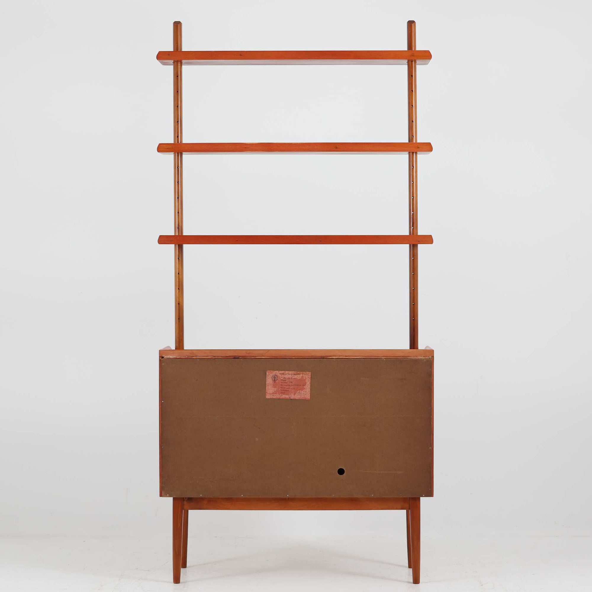 スウェーデンの老舗家具メーカー、Svenssons Mobler社によるマホガニー材のディスプレイシェルフです。上部の3段シェルフは高さを調整できる可動棚仕様で、書籍やオブジェ、植物などをバランス良く飾ることができます。下段のスライド扉収納は実用性が高く、生活感をすっきりと隠せる構造です。滑らかな木肌と温かみのある赤褐色の木目がマホガニーならではの上品な雰囲気を醸し出します。脚部の細身なテーパー形状も美しく、空間に軽やかさを添える北欧ビンテージ家具です。スライド扉の取っ手部分は丸くくり抜かれており、シンプルながらも洗練された印象を与えます。収納部と棚板の両サイドに開けられた穴に支柱を通して組み立てる独特の構造が特徴で、機能性とデザイン性を兼ね備えたスウェーデンらしい巧みな造りです。
