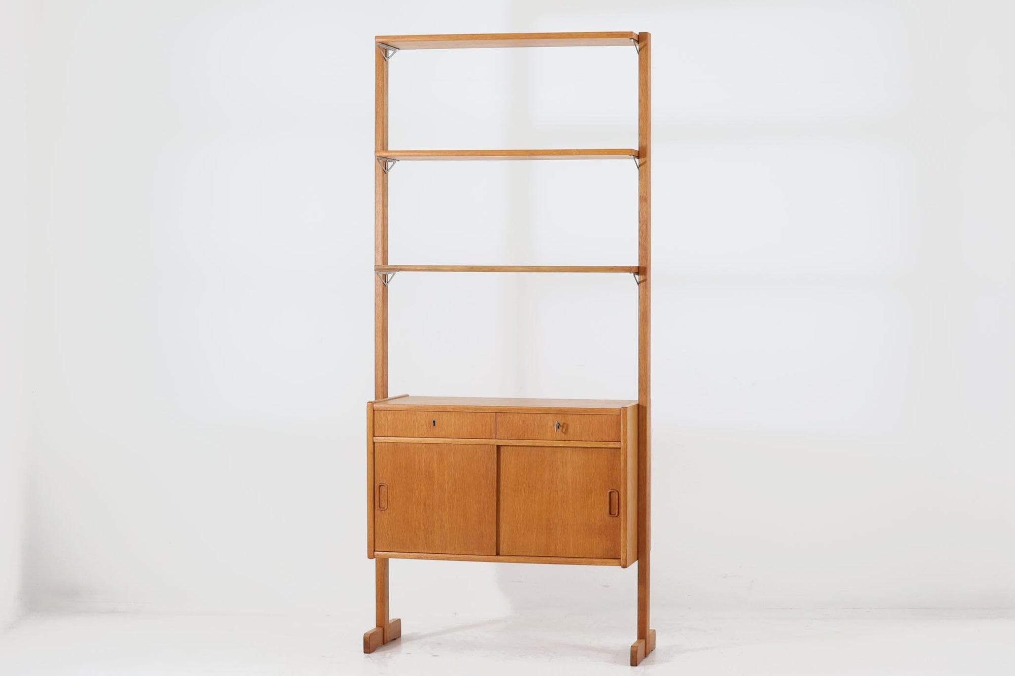 こちらはスウェーデンから買い付けたディスプレイシェルフです。背面にもオーク材が使用されているため、お部屋の中央に置き、間仕切りとしてもお使いいただける設計となっています。棚は中央に脚が配置されているため物の出し入れの際に邪魔にならず、また横から見たデザインがシンメトリーになっています。良質なオーク材が使用されており、経年により深みを増した色味が、このシェルフの魅力の一つです。