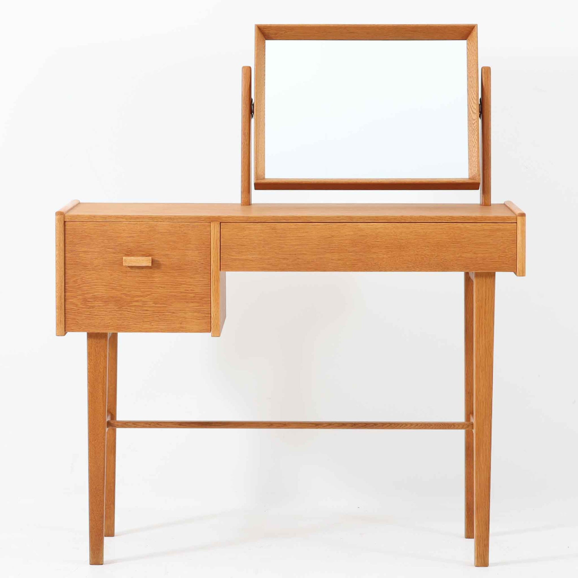 スウェーデンのSvenska Mobelfabrikerna社によって製造されたこちらのドレッサーは、ミニマルで洗練されたフォルムと、上質なオーク材の温もりが魅力の北欧ビンテージ家具です。直線的なフレームで構成されたミラーは本体にすっきりと収まり、使わない時には視線を遮らず空間に軽やかさをもたらします。左右非対称に配された引き出しは、小物類をすっきりと収納でき、実用性にも優れています。細身の脚部と貫による構造美も印象的で、経年により味わいを増した木肌が空間に落ち着きと趣を与えてくれます。北欧ビンテージ家具ならではの質感と静かな存在感を兼ね備えた一台です。