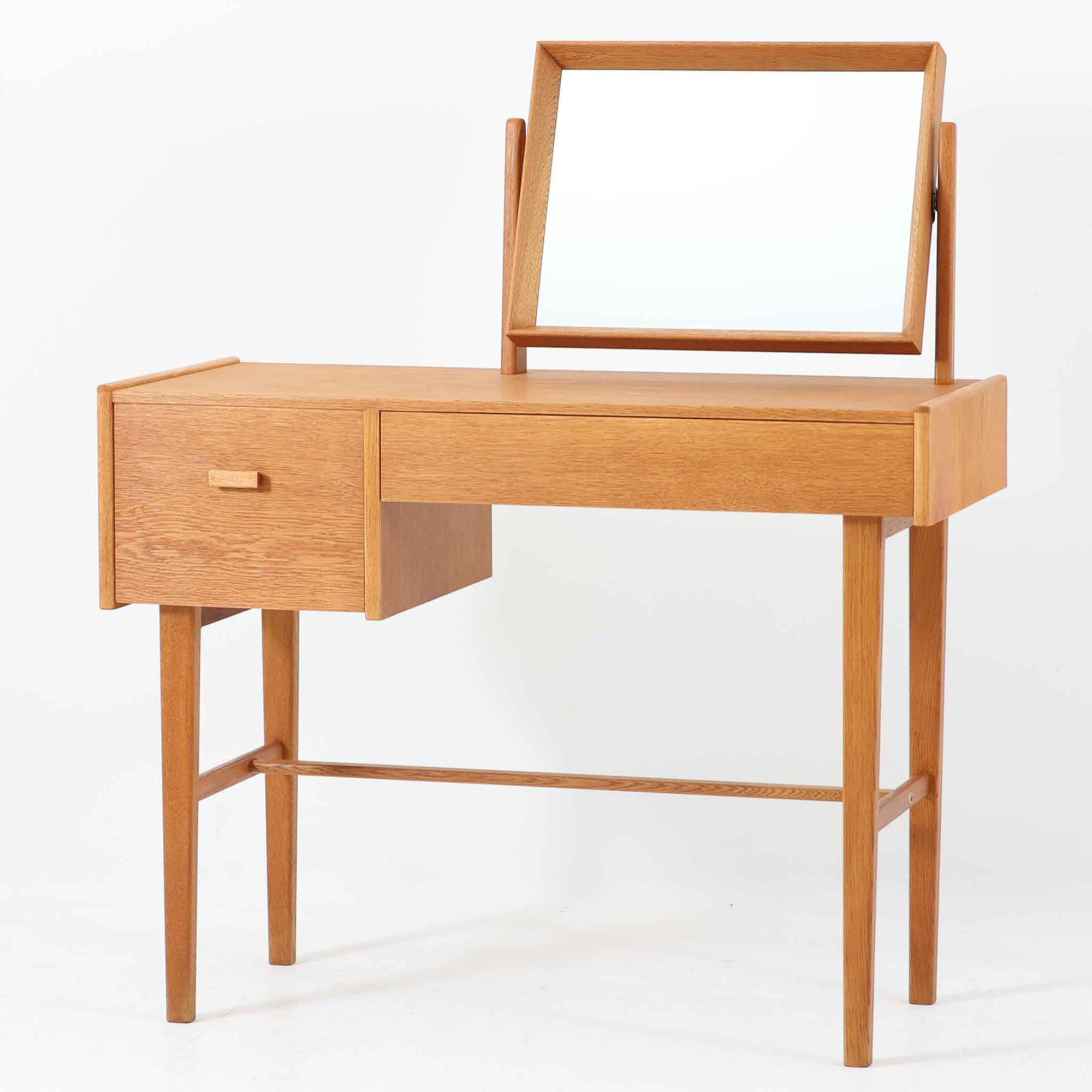 スウェーデンのSvenska Mobelfabrikerna社によって製造されたこちらのドレッサーは、ミニマルで洗練されたフォルムと、上質なオーク材の温もりが魅力の北欧ビンテージ家具です。直線的なフレームで構成されたミラーは本体にすっきりと収まり、使わない時には視線を遮らず空間に軽やかさをもたらします。左右非対称に配された引き出しは、小物類をすっきりと収納でき、実用性にも優れています。細身の脚部と貫による構造美も印象的で、経年により味わいを増した木肌が空間に落ち着きと趣を与えてくれます。北欧ビンテージ家具ならではの質感と静かな存在感を兼ね備えた一台です。