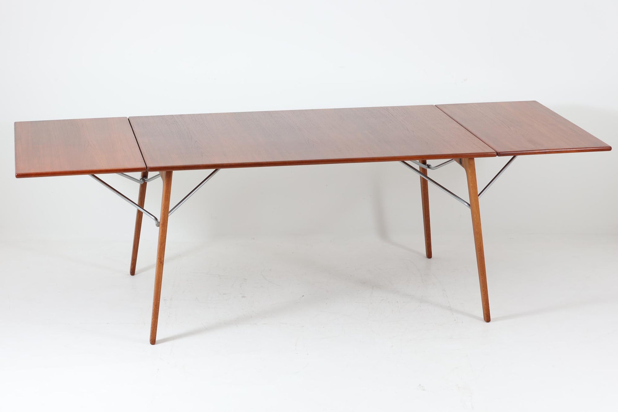 北欧から買い付けた、Børge mogensenデザインのmodel 162です。「DESIGN mUSEUm DANmARK」によれば、このモデルは1953年にデザインされたものです。Børge mogensenの作品としては珍しく、金属と木材を組み合わせたデザインが特徴です。天板には、色味の濃い高品質なチーク材が使用され、脚部はナチュラルな色合いのスリムなデザインが採用されています。また、補強材として使用されたスチールの色合いとの調和により、全体的に非常に洗練された印象を与えつつも、スチールにより高い強度が確保されています。天板中央のビスを外すことで、テーブルは折り畳み可能となり、引っ越し時の搬入や搬出も安心して行えます。