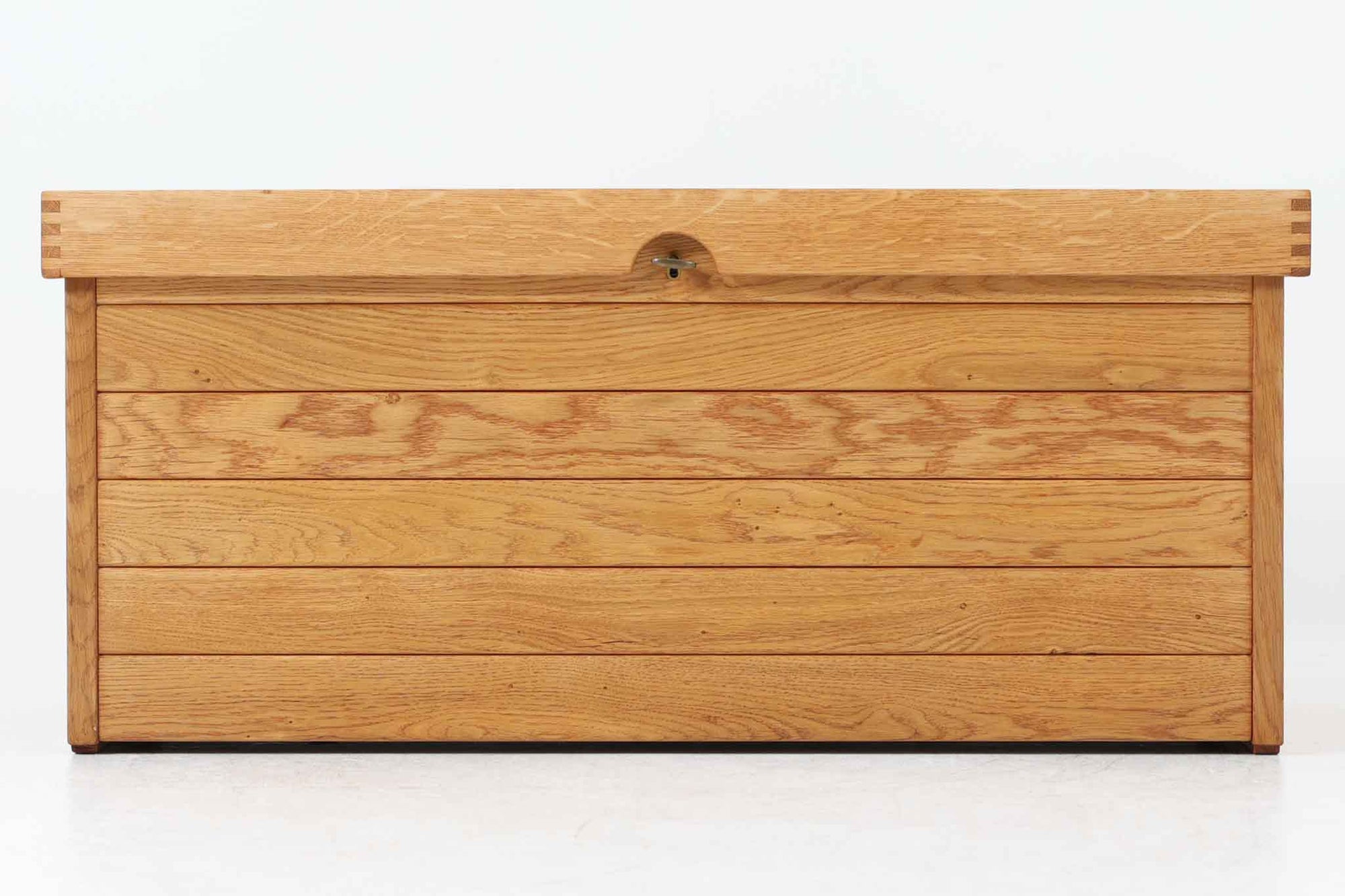 Kai Kristiansenデザインのチェストです。1960〜1970年代にデザインされた当時にはチェストは既に現代のような引き出し付きの形状が一般的でした。しかし、それよりも以前の時代にはチェストはトランクのような形状で、腰掛けるベンチやテーブルとしても使える多用途な家具でした。このチェストも、そのような昔のデザインを基に作られたのではないかと考えられます。堅牢なオーク無垢材で作られたこのチェストには、真鍮製の蝶番式の蓋と鍵が付属しており、外側には持ち運びのために両側に2つのハンドルが備えられています。元々は収納内部に小さいトレーがあった様ですが、こちらは欠品しています。