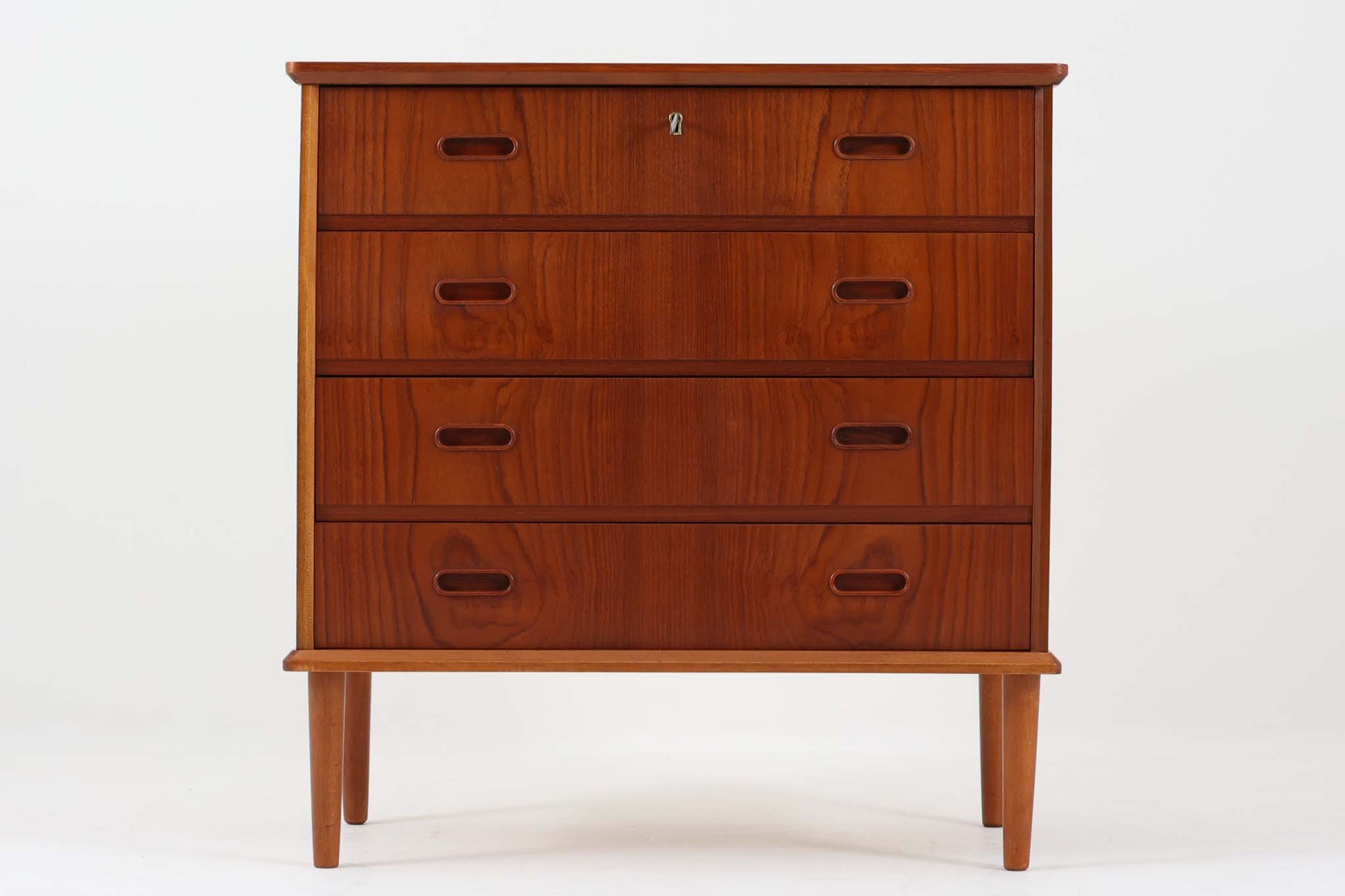 シンプルながらも洗練されたデザインが魅力の、デンマーク製ビンテージチェスト。温かみのある木目が美しいチーク材が使用され、深みのある色合いが上品な印象を与えます。4段の引き出しは収納力があり、上段には鍵付きの収納スペースを備え、実用性にも優れています。引き出しの持ち手は彫り込み式になっており、すっきりとしたデザインの中に北欧家具らしいディテールが光ります。丸みを帯びたテーパードレッグが軽やかな印象を与え、どんな空間にも馴染みやすい一台。北欧ヴィンテージならではの美しい造りと機能性を兼ね備えた、魅力的な収納家具です。
