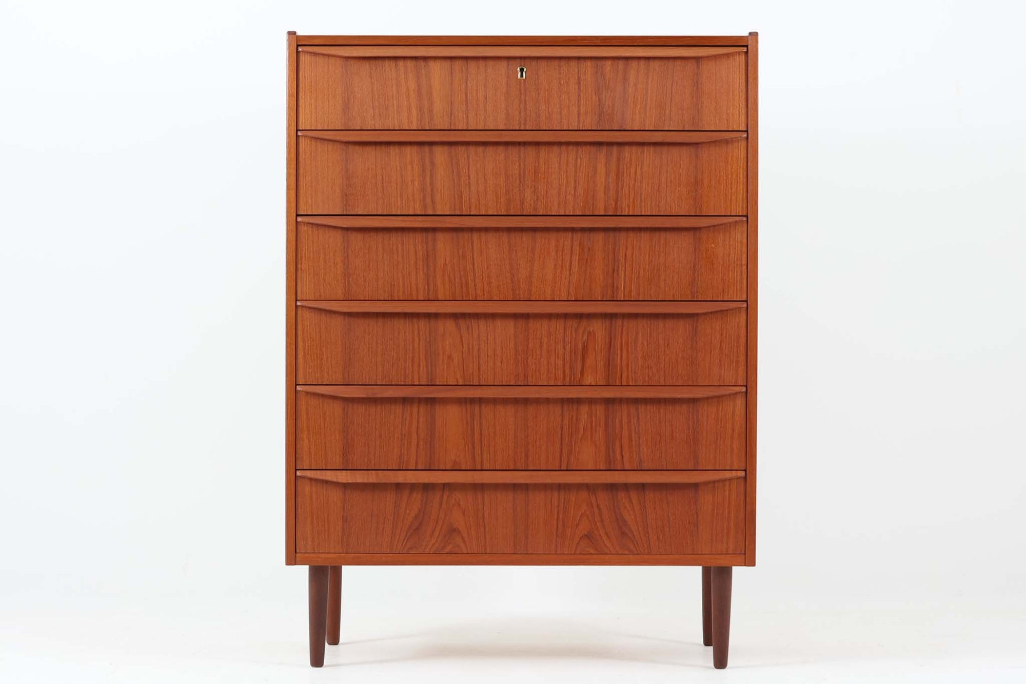 デンマーク製のビンテージ6段チェストのご紹介です。チーク材特有の温かみある木目が美しく、北欧家具らしい洗練された佇まいが魅力の一台です。前板には彫り込み式の取手が施され、無駄を省いたミニマルなデザインが印象的。すっきりとしたフォルムと丸脚のバランスも良く、リビングや寝室など様々な空間に自然と馴染みます。6杯の引き出しはすべてスムーズに開閉でき、収納力も十分。天板には縁が設けられており、小物のディスプレイにも適しています。