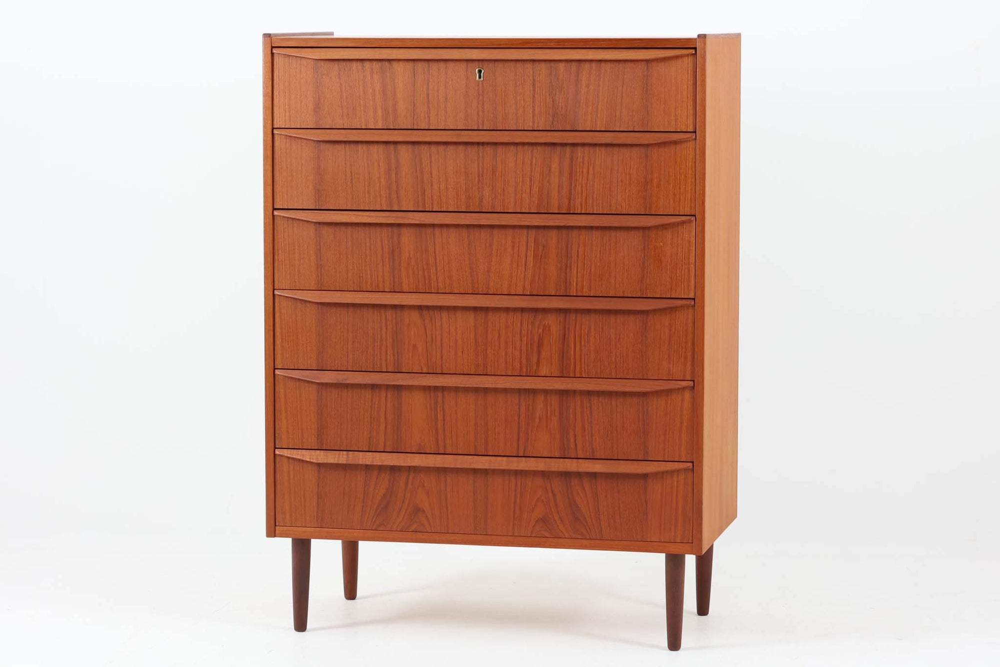 デンマーク製のビンテージ6段チェストのご紹介です。チーク材特有の温かみある木目が美しく、北欧家具らしい洗練された佇まいが魅力の一台です。前板には彫り込み式の取手が施され、無駄を省いたミニマルなデザインが印象的。すっきりとしたフォルムと丸脚のバランスも良く、リビングや寝室など様々な空間に自然と馴染みます。6杯の引き出しはすべてスムーズに開閉でき、収納力も十分。天板には縁が設けられており、小物のディスプレイにも適しています。