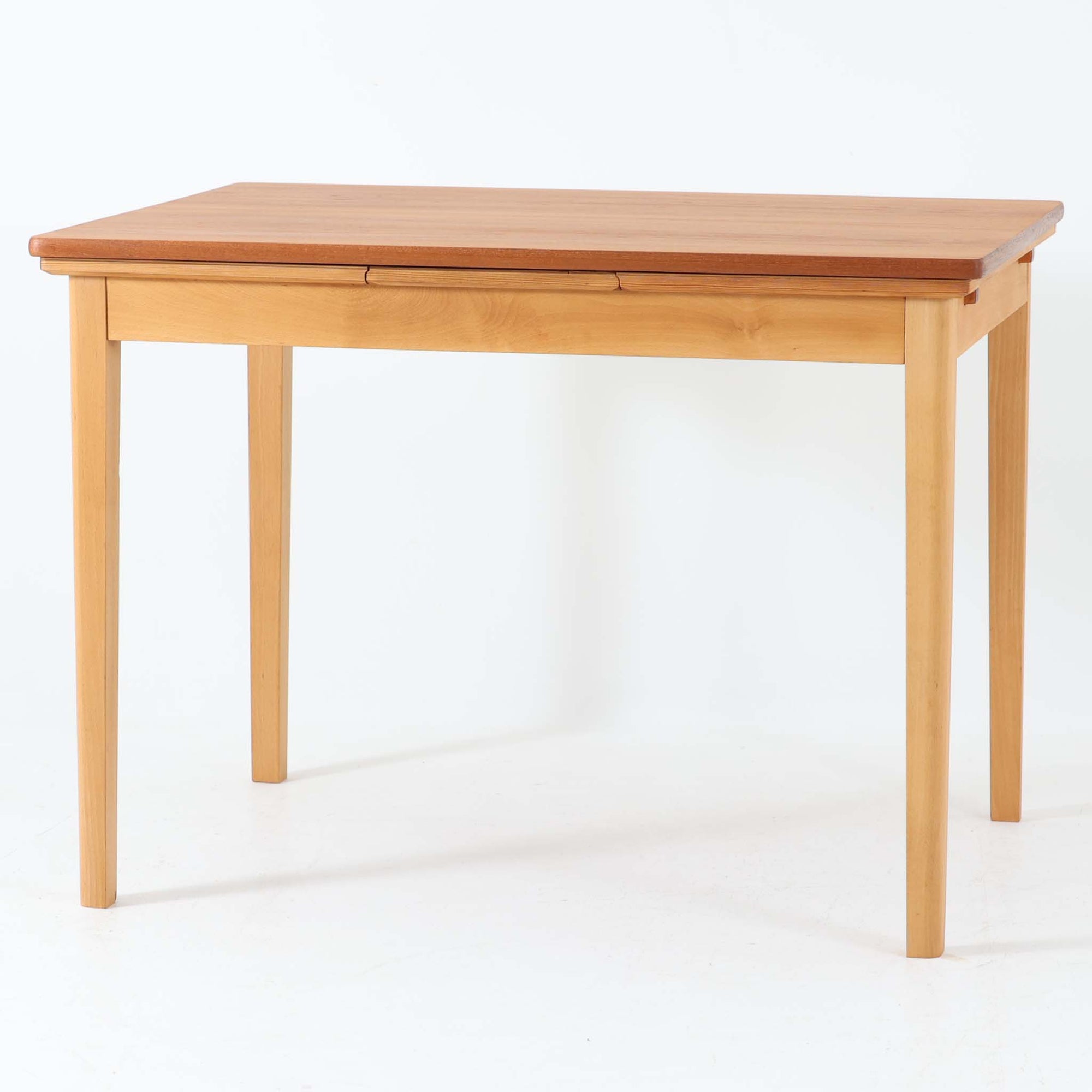 チーク材とビーチ材を組み合わせたデンマーク製のエクステンションダイニングテーブル。天板には深みのあるチーク材、脚部、幕板、拡張板には明るいビーチ材を使用し、異素材のコントラストが洗練された印象を与えます。幅100cmとコンパクトながら、両側に伸長式リーフを備え、用途に応じて天板の拡張が可能。シンプルで堅牢なつくりは、限られた空間にもフィットし、経年変化による木材の味わいとともに、長く愛用できる北欧ビンテージ家具の魅力が詰まった一台です。