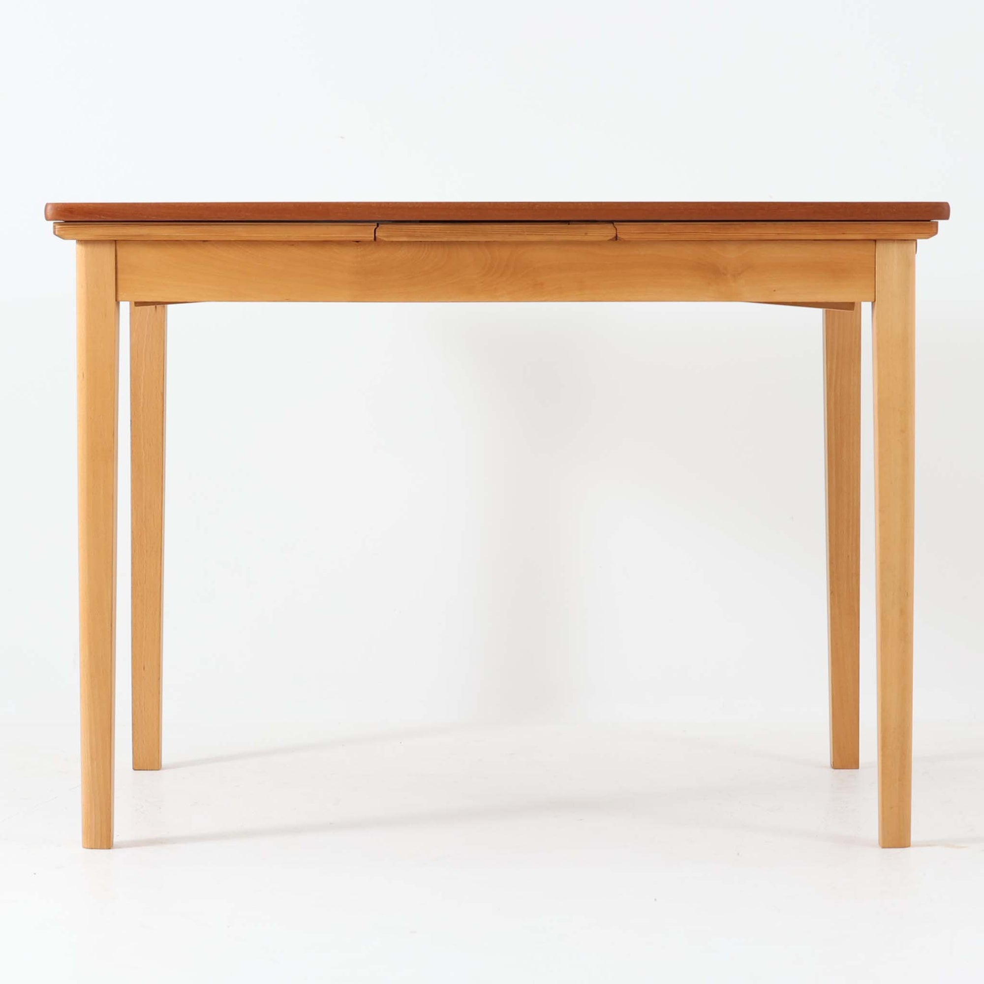 チーク材とビーチ材を組み合わせたデンマーク製のエクステンションダイニングテーブル。天板には深みのあるチーク材、脚部、幕板、拡張板には明るいビーチ材を使用し、異素材のコントラストが洗練された印象を与えます。幅100cmとコンパクトながら、両側に伸長式リーフを備え、用途に応じて天板の拡張が可能。シンプルで堅牢なつくりは、限られた空間にもフィットし、経年変化による木材の味わいとともに、長く愛用できる北欧ビンテージ家具の魅力が詰まった一台です。