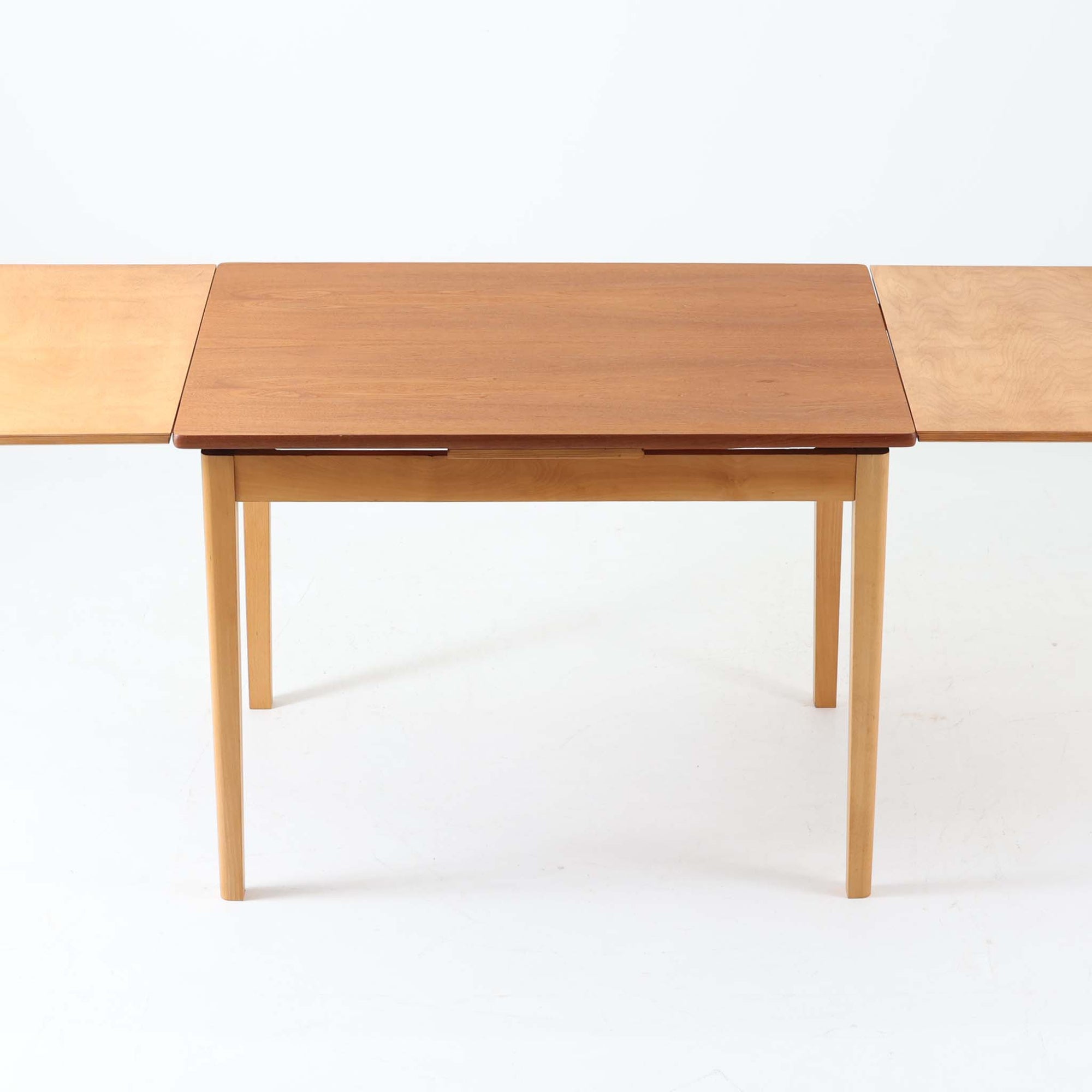 チーク材とビーチ材を組み合わせたデンマーク製のエクステンションダイニングテーブル。天板には深みのあるチーク材、脚部、幕板、拡張板には明るいビーチ材を使用し、異素材のコントラストが洗練された印象を与えます。幅100cmとコンパクトながら、両側に伸長式リーフを備え、用途に応じて天板の拡張が可能。シンプルで堅牢なつくりは、限られた空間にもフィットし、経年変化による木材の味わいとともに、長く愛用できる北欧ビンテージ家具の魅力が詰まった一台です。