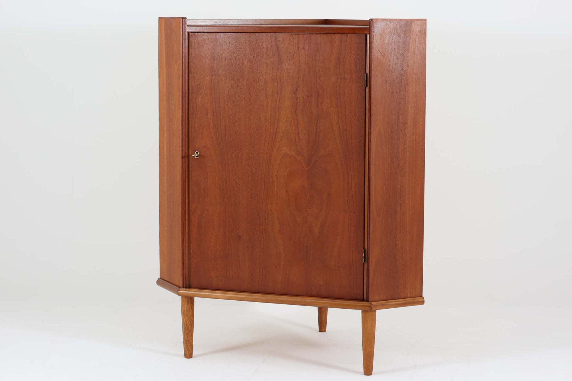 デンマーク製のコーナーキャビネットです。本体には良質なチーク材が贅沢に使用されており、脚部にはオーク材が用いられた異素材の組み合わせが魅力的です。扉はガラスがなく中が見えないシンプルなデザインで、チーク材の美しい木目を存分に楽しめます。コンパクトなコーナーデザインは空間を有効活用でき、天板の縁には物が落ちにくいよう立ち上がりが施されているため、飾り付けにも適しています。錠前は破損しており施錠はできませんが、扉はボールキャッチで固定され、スムーズに開閉します。シンプルながらも機能性とデザイン性を兼ね備えた一品です。