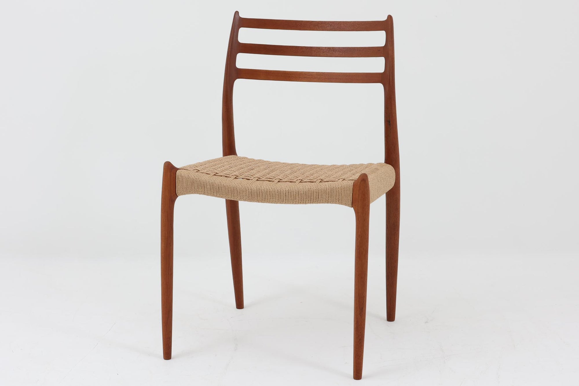 デンマークJ.L. moller社製のmodel 78チェアです。フレームには良質なチーク材が使用され、細いラインが組み合わさった工芸作品のような佇まいが魅力です。背もたれの美しいカーブや広めの座面により快適な座り心地を実現し、背もたれのラインは掃除の際に手を掛けやすく、使い勝手も優れています。座面には耐久性のあるペーパーコードを使用しており、張り替え済みのため清潔で快適にお使いいただけます。長く使用しても張替えが可能なため、世代を超えてご愛用いただけます。現行品でもチーク材モデルは販売されていますが、資材の入手が難しくなり、メーカー廃盤予定のため、今後はビンテージ品でのみ入手可能となる希少な一脚です。