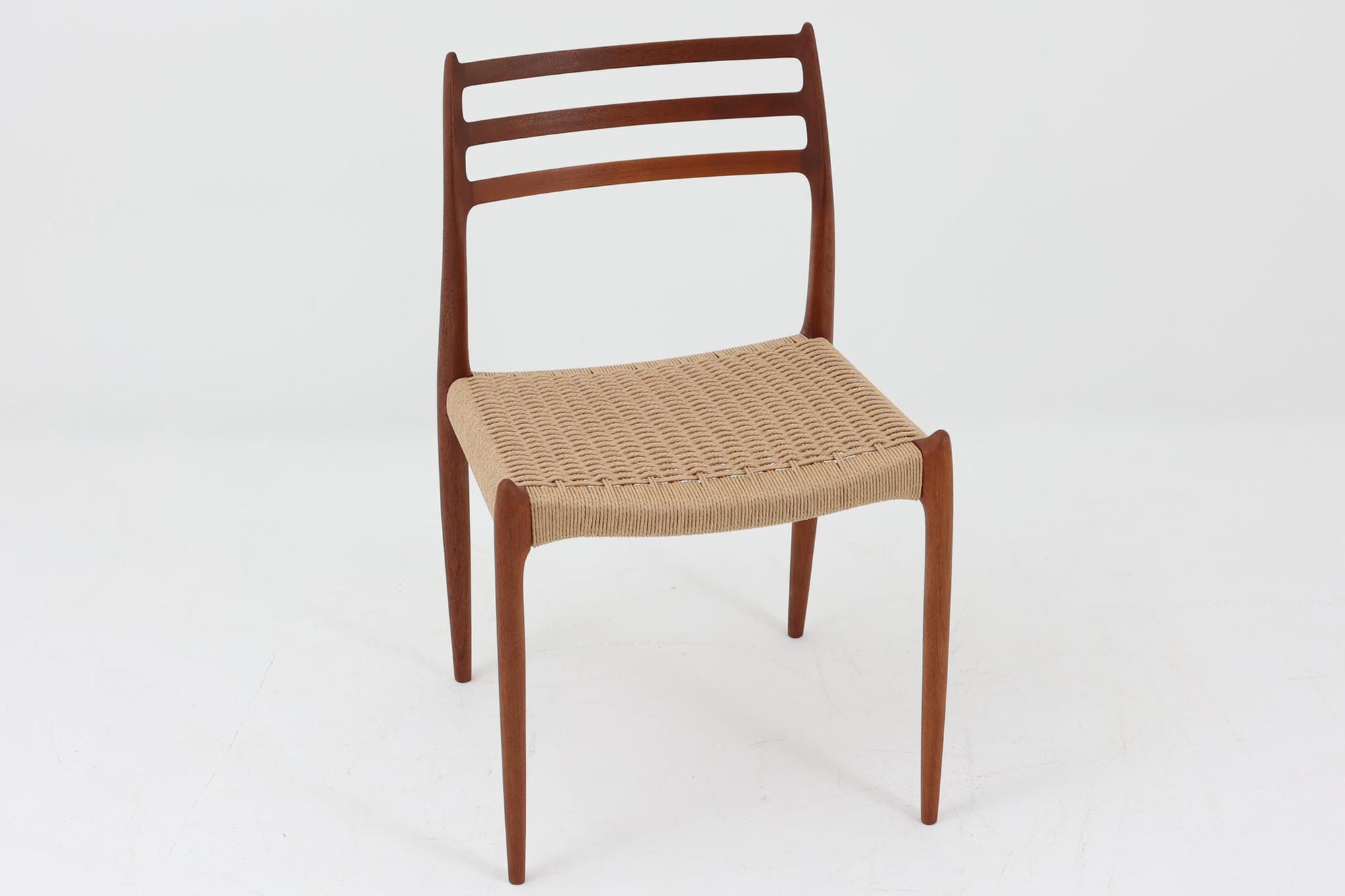 デンマークJ.L. moller社製のmodel 78チェアです。フレームには良質なチーク材が使用され、細いラインが組み合わさった工芸作品のような佇まいが魅力です。背もたれの美しいカーブや広めの座面により快適な座り心地を実現し、背もたれのラインは掃除の際に手を掛けやすく、使い勝手も優れています。座面には耐久性のあるペーパーコードを使用しており、張り替え済みのため清潔で快適にお使いいただけます。長く使用しても張替えが可能なため、世代を超えてご愛用いただけます。現行品でもチーク材モデルは販売されていますが、資材の入手が難しくなり、メーカー廃盤予定のため、今後はビンテージ品でのみ入手可能となる希少な一脚です。