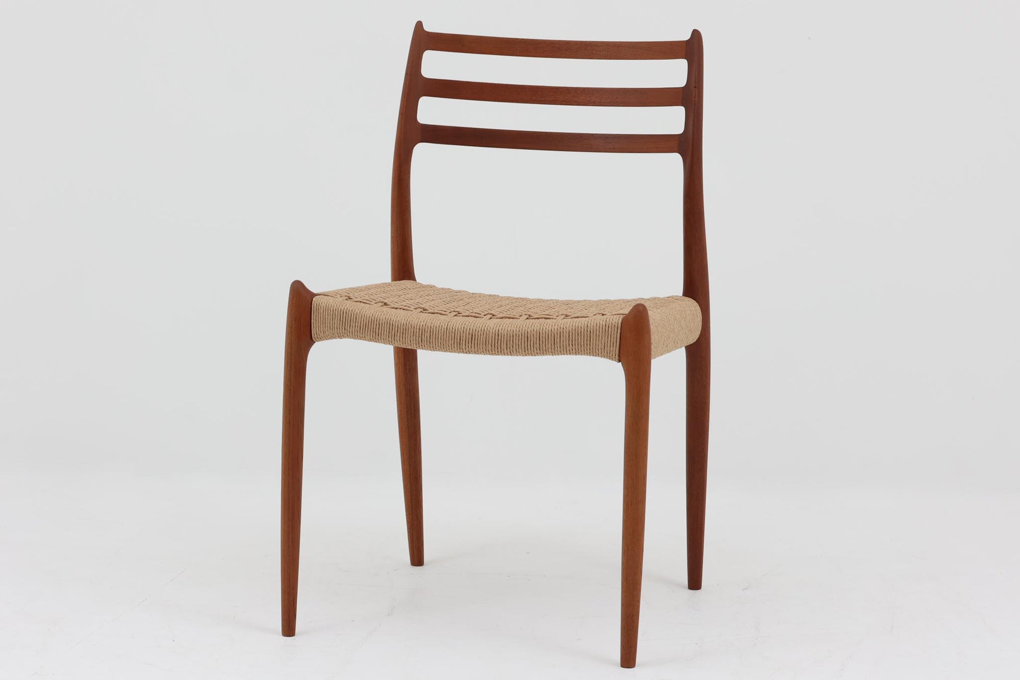 デンマークJ.L. moller社製のmodel 78チェアです。フレームには良質なチーク材が使用され、細いラインが組み合わさった工芸作品のような佇まいが魅力です。背もたれの美しいカーブや広めの座面により快適な座り心地を実現し、背もたれのラインは掃除の際に手を掛けやすく、使い勝手も優れています。座面には耐久性のあるペーパーコードを使用しており、張り替え済みのため清潔で快適にお使いいただけます。長く使用しても張替えが可能なため、世代を超えてご愛用いただけます。現行品でもチーク材モデルは販売されていますが、資材の入手が難しくなり、メーカー廃盤予定のため、今後はビンテージ品でのみ入手可能となる希少な一脚です。