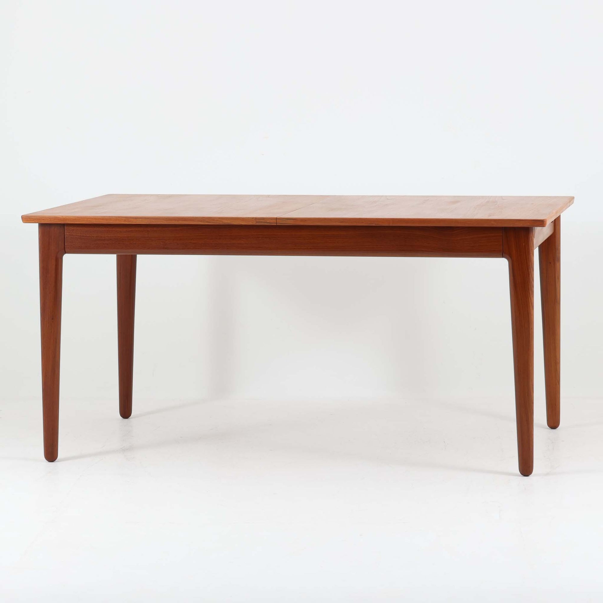Vamo Mobelfabrikによって製造されたこちらのエクステンションダイニングテーブルは、チーク材の豊かな木目と重厚感のある質感が魅力の北欧ビンテージ家具で、幅150cmから最大270cmまで拡張可能な構造により、来客時や家族団らんの場にも柔軟に対応します。天板下に格納された2枚の中板を引き出して使用するシステムは実用性と美しさを兼ね備え、シャープなエッジと丸みを帯びた脚部が洗練された佇まいを演出します。デザイナー不明ながら、Vamo社ならではの確かな造りとDanish Controlラベルが品質の高さを物語る一台です。
