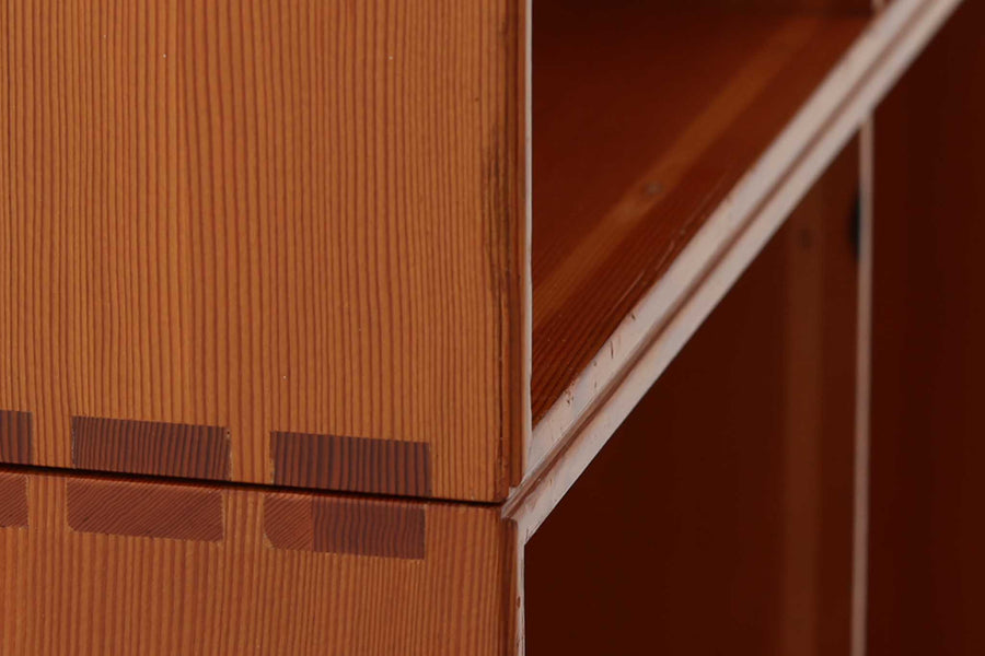こちらは、1928年にmogens Kochによってデザインされた家具です。この家具には合板ではなく無垢材が使用されており、割れや狂いを防ぐためにさまざまな工夫が施されています。使用されているのは、良質で狂いが少ないパイン材の中でも、特に耐久性と強度に優れたオレゴンパインの無垢材が使用されています。経年変化によって深みを増した色味が魅力的な一点となっています。もともとは書斎用にデザインされたもので、扉付きキャビネットや奥行きの浅い棚など、好みに応じて組み合わせて使用できるシステムシェルフとして設計されています。そのため、ヴィンテージ家具市場では多様な組み合わせの形で見られることが特徴です。こちらの商品は、シンプルな台輪とシェルフ2点を組み合わせた構成となっています。